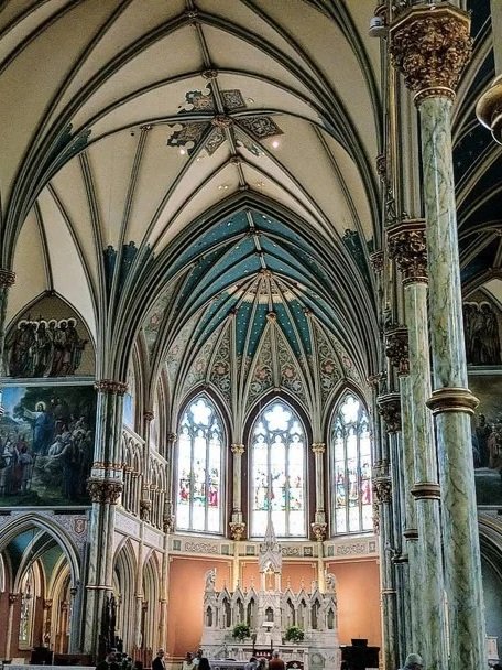 Interior of a Gothic-style church with pointed arches, stained glass windows, and ornate columns.