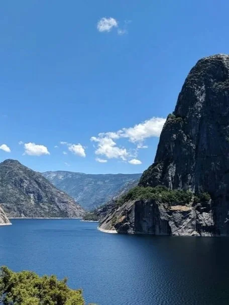 A large body of water surrounded by mountain cliffs under a blue sky with scattered clouds.