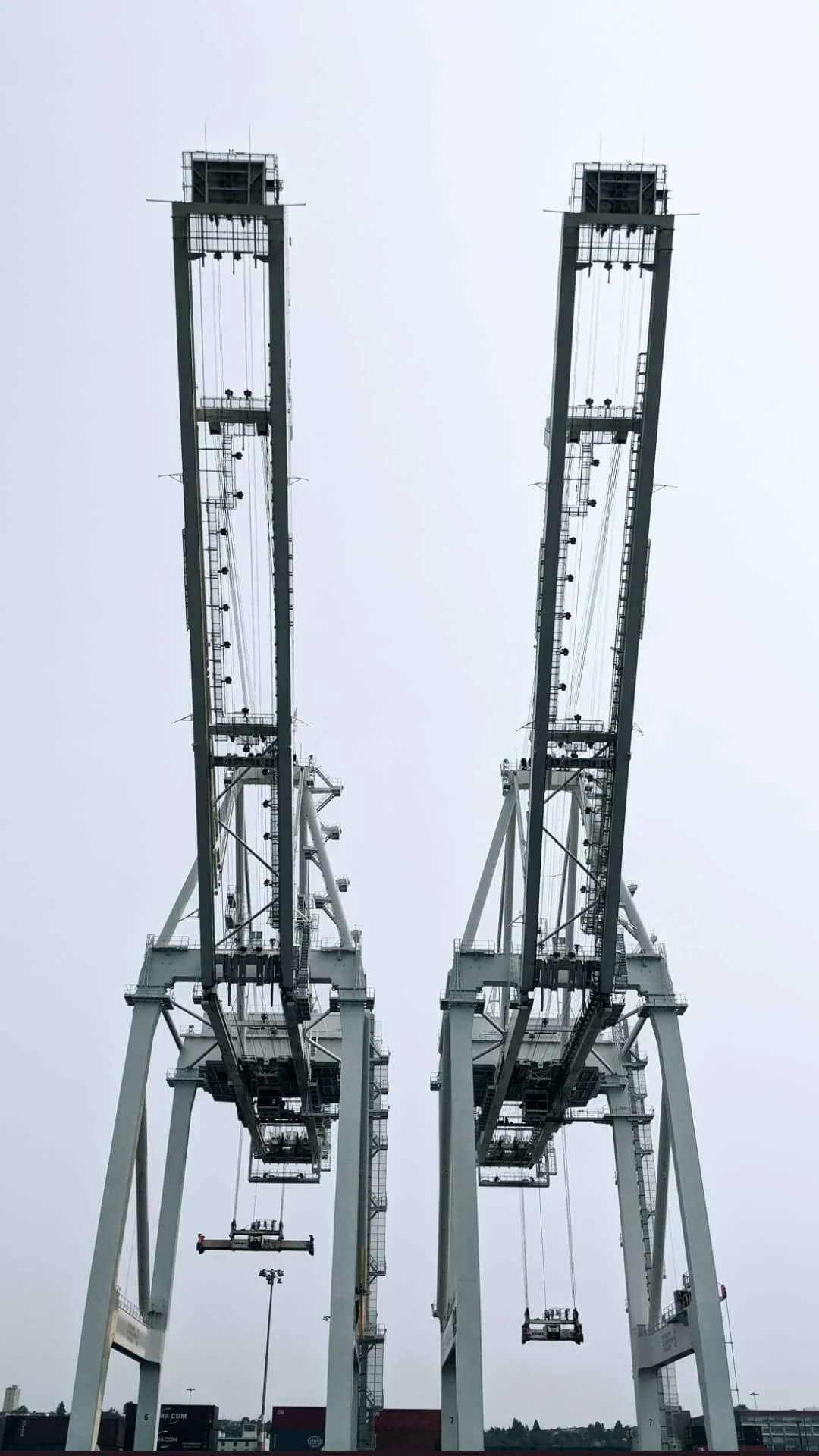 Two large industrial gantry cranes standing side by side against a gray, overcast sky at a port.