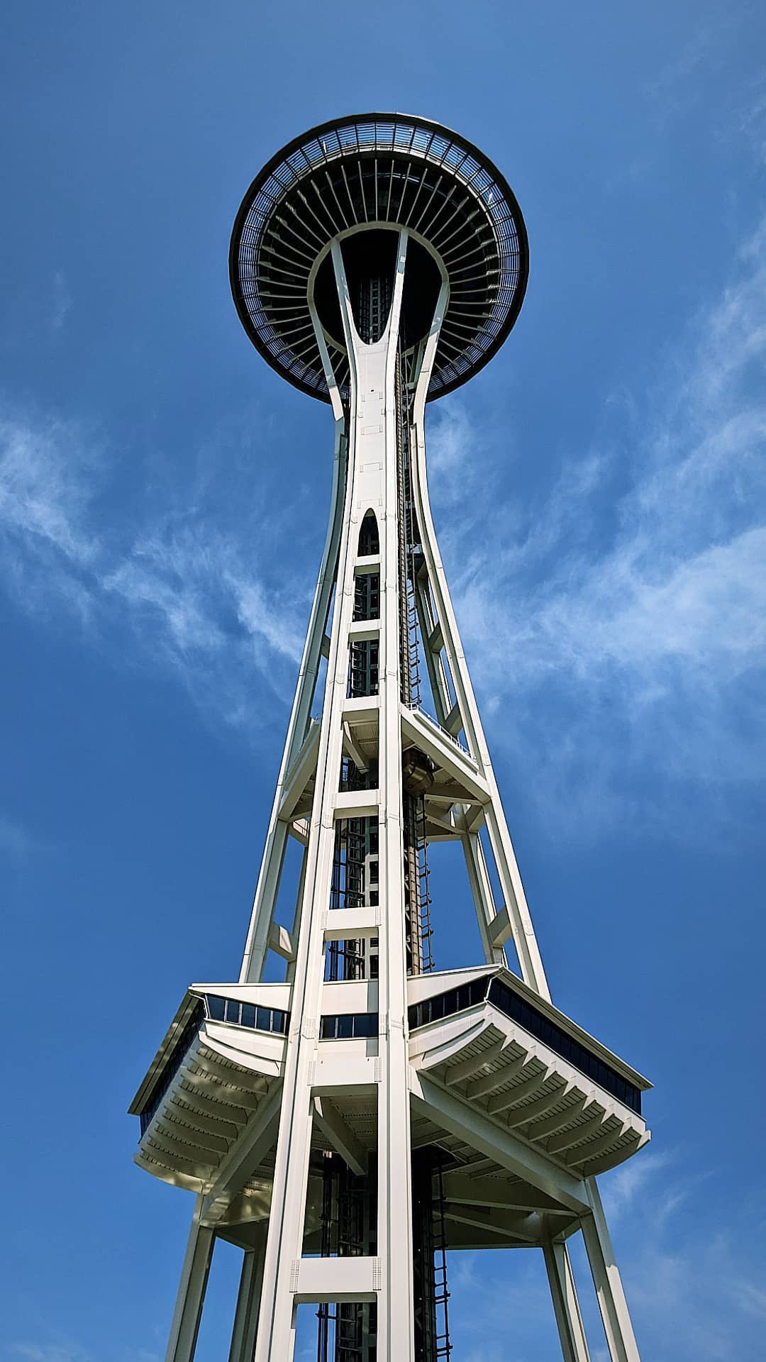 A tall observation tower with a circular viewing platform at the top, standing against a blue sky with some clouds.
