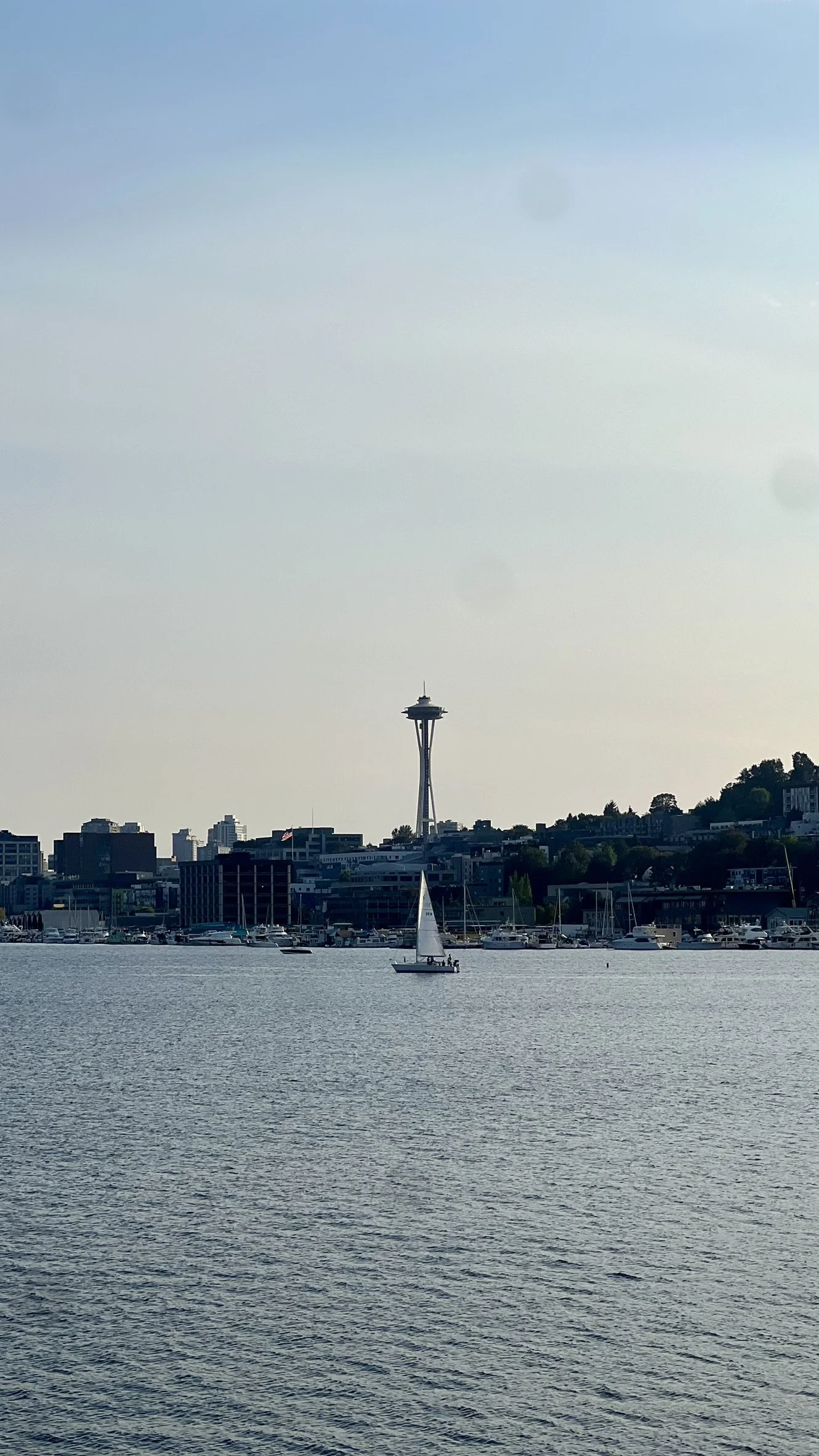 A sailboat on calm water with the Seattle Space Needle and city skyline in the background.
