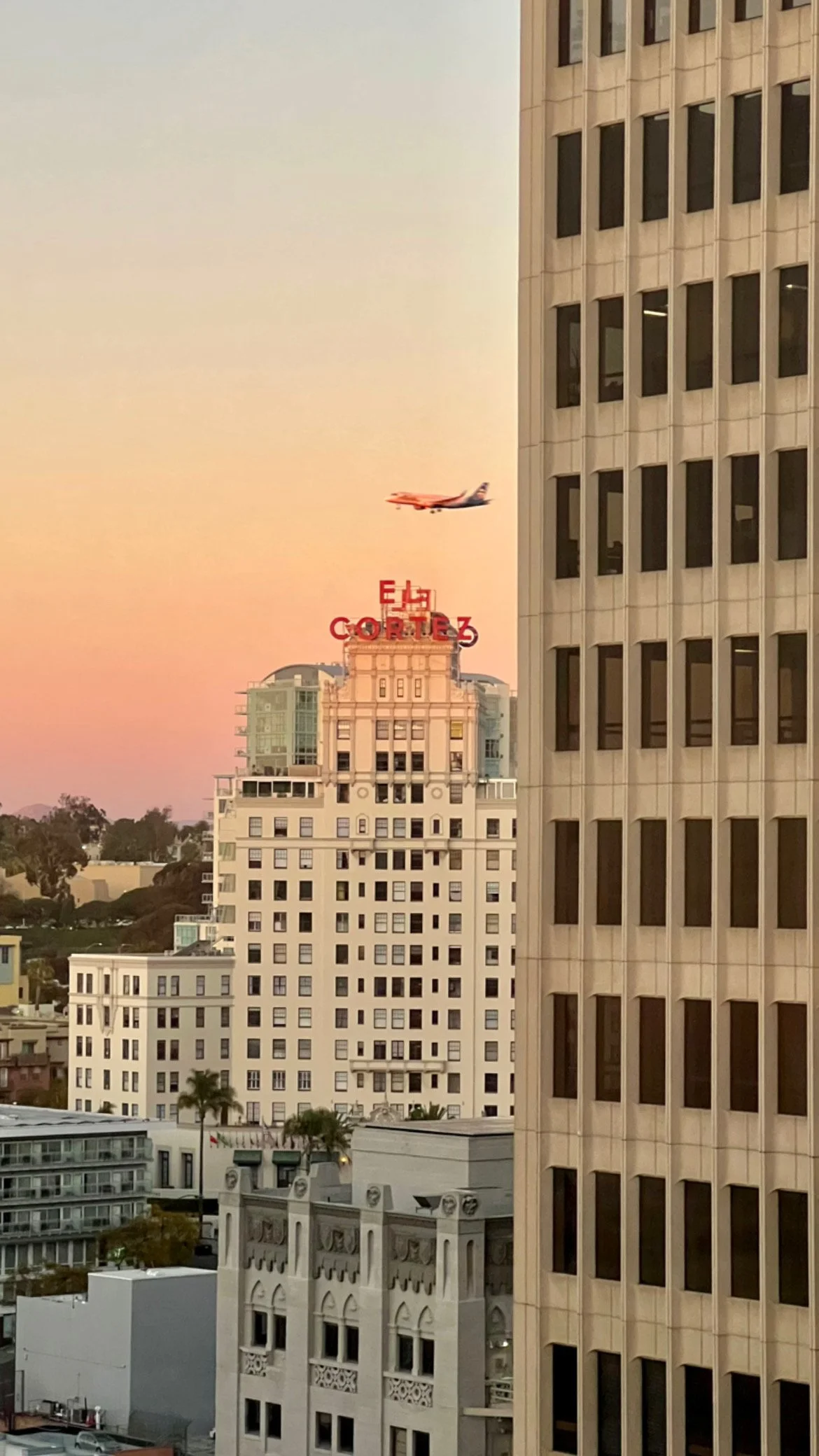 Skyline of tall buildings in an urban area with an airplane flying overhead during sunset.