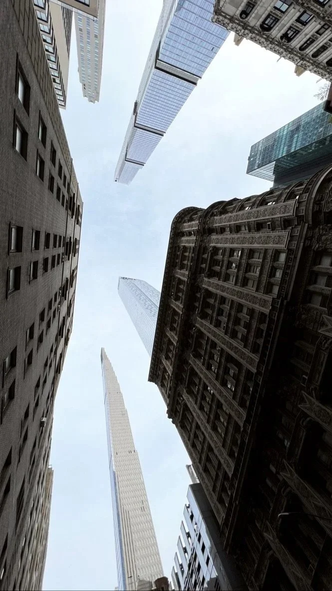 Looking up at tall skyscrapers in a city, with clear sky visible between the buildings.