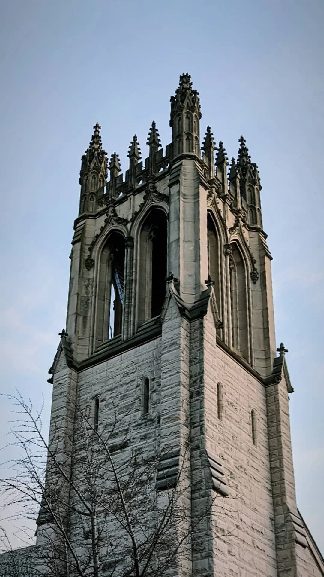 A tall, pointed Gothic-style tower with ornate stonework and arched windows, set against a light blue sky.