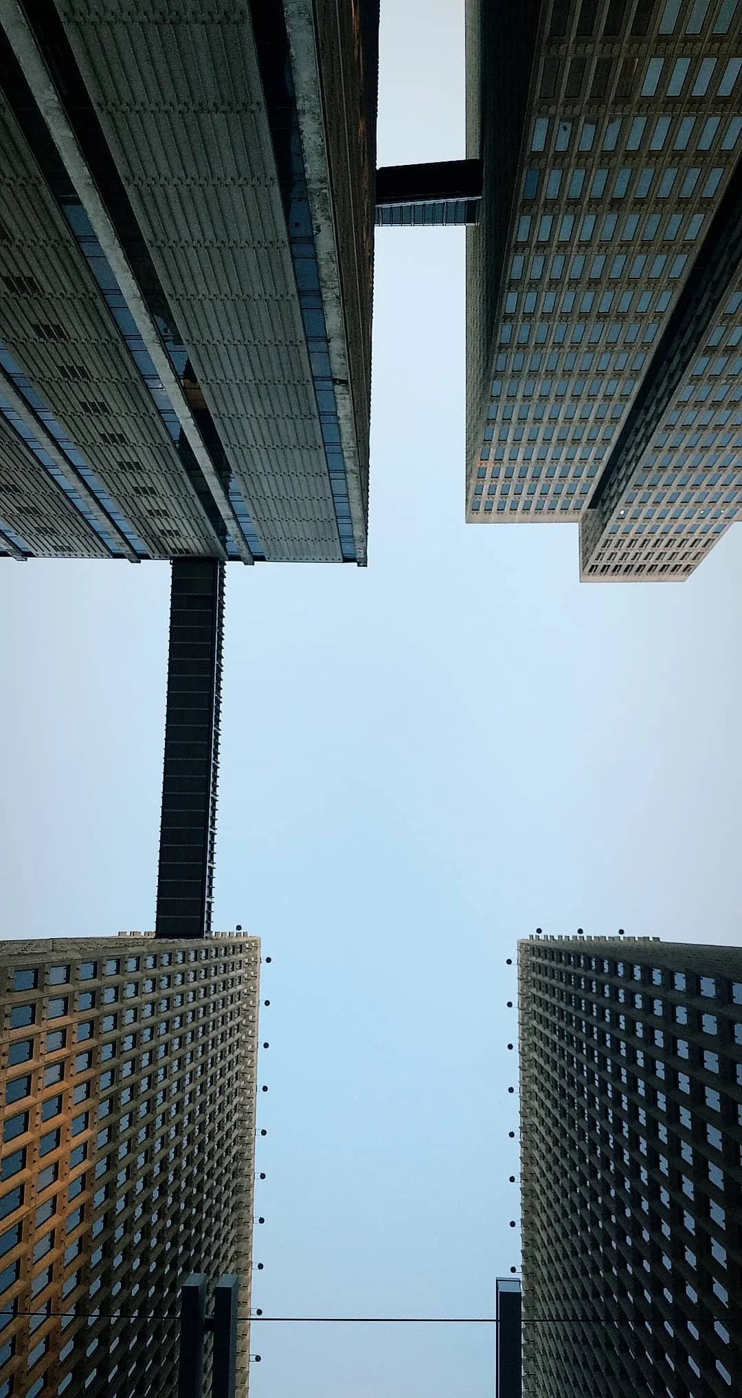 Looking up at four tall modern skyscrapers with a clear sky above, connected by sky bridges and featuring numerous windows.