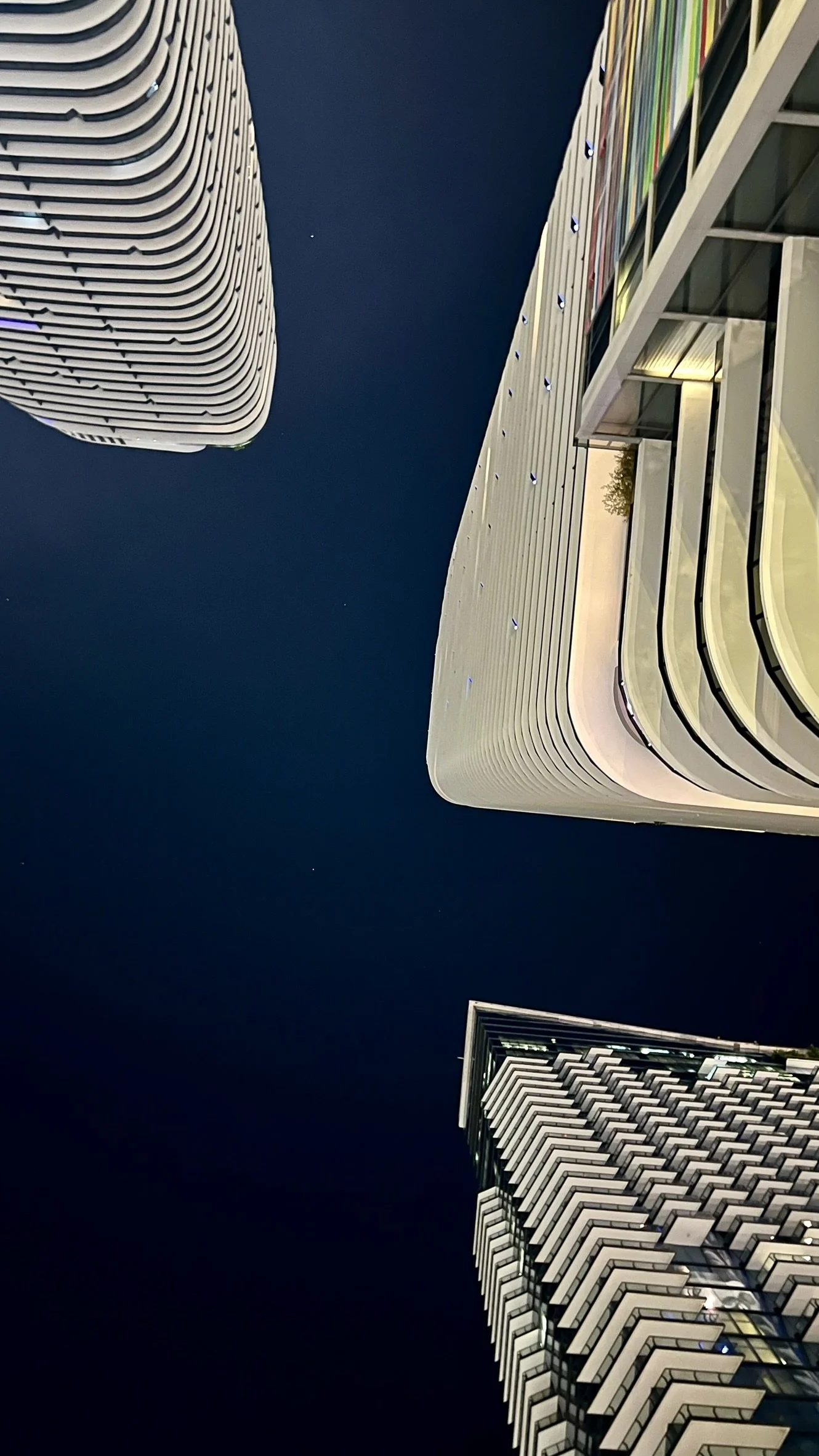 Nighttime view of three tall modern buildings with unique architectural designs against a dark sky.