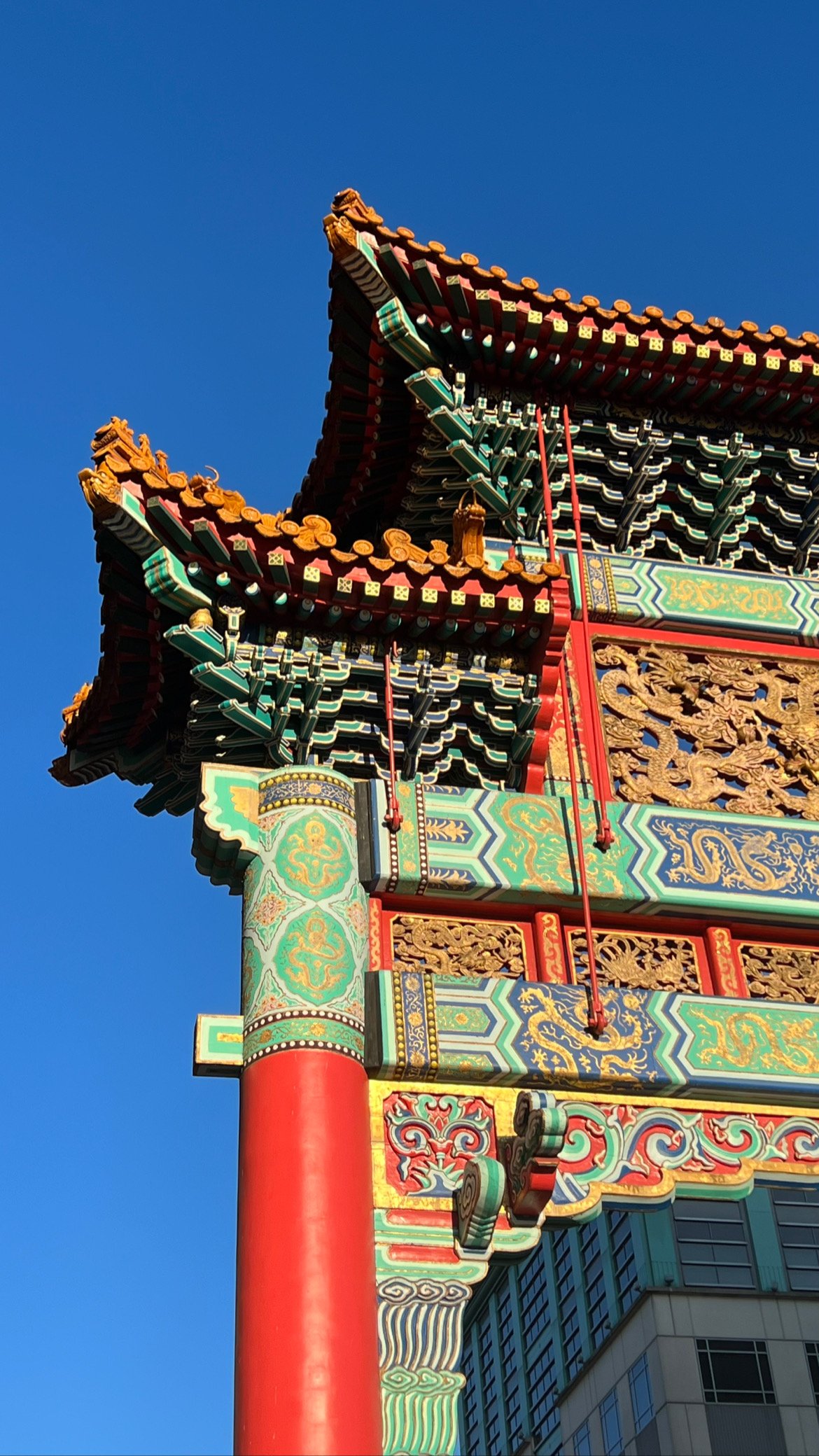 Close-up of traditional Chinese architectural details on a colorful structure, featuring ornate carvings, decorative roofing, and painted patterns against a clear blue sky.