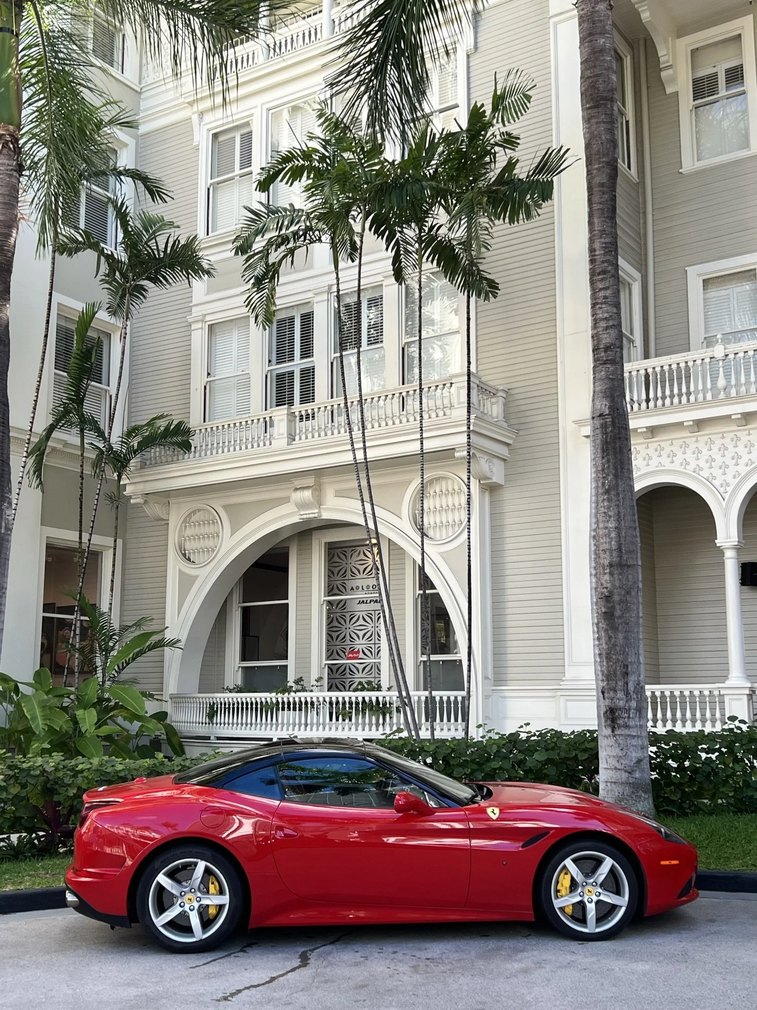 Red Ferrari convertible parked in front of a white multi-story building with palm trees.
