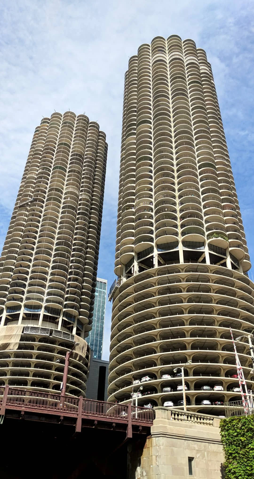 Two tall, cylindrical skyscrapers with rounded balconies, one with parked cars on lower levels, set against a blue sky.