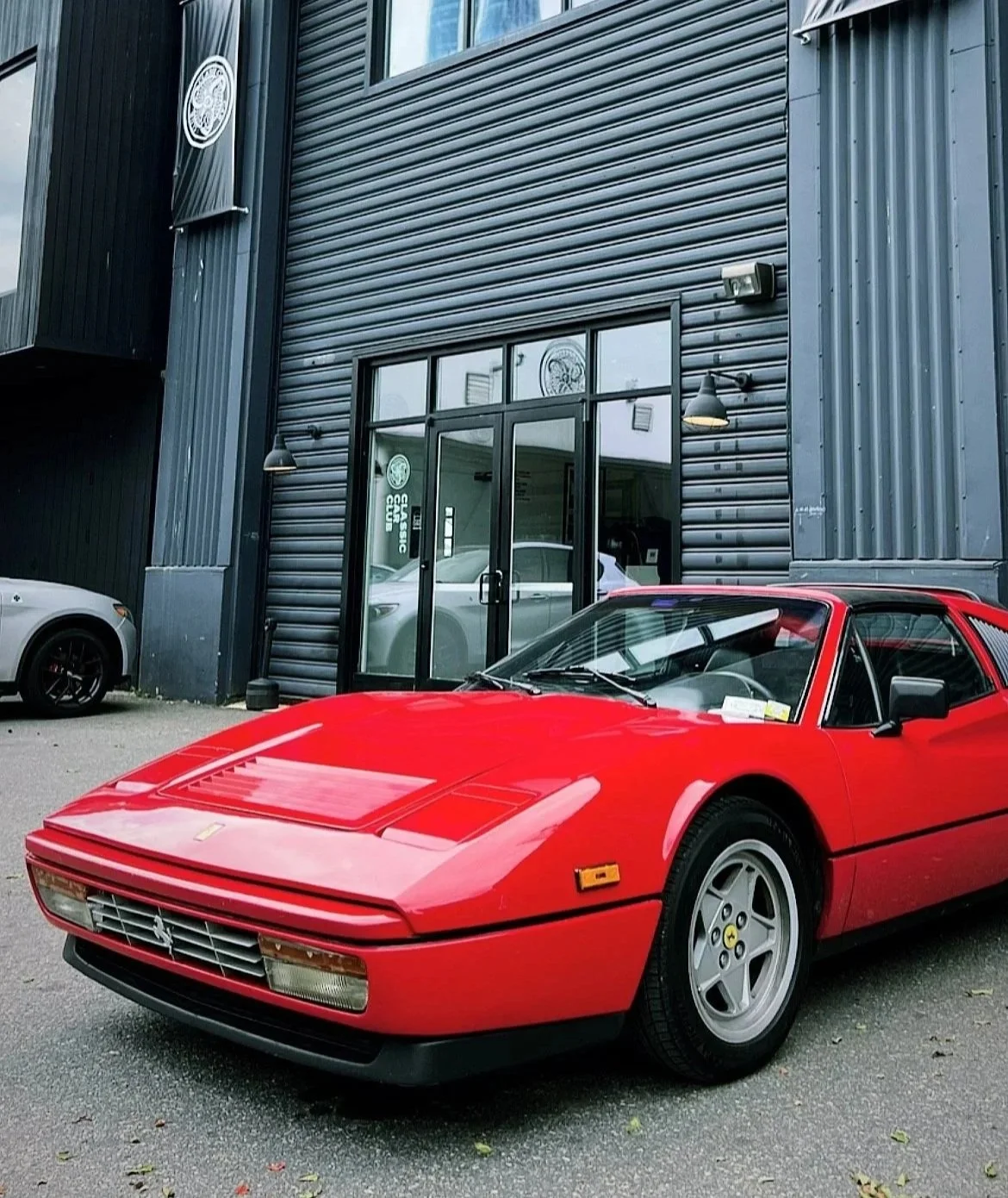 Red vintage Ferrari sports car parked outside a modern building with black metal siding and glass doors.