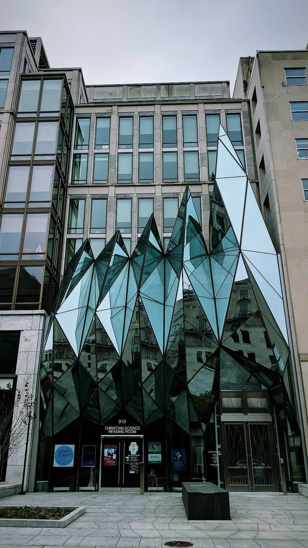 Modern building with a glass facade featuring angular, faceted glass panels, reflecting nearby buildings and the sky.
