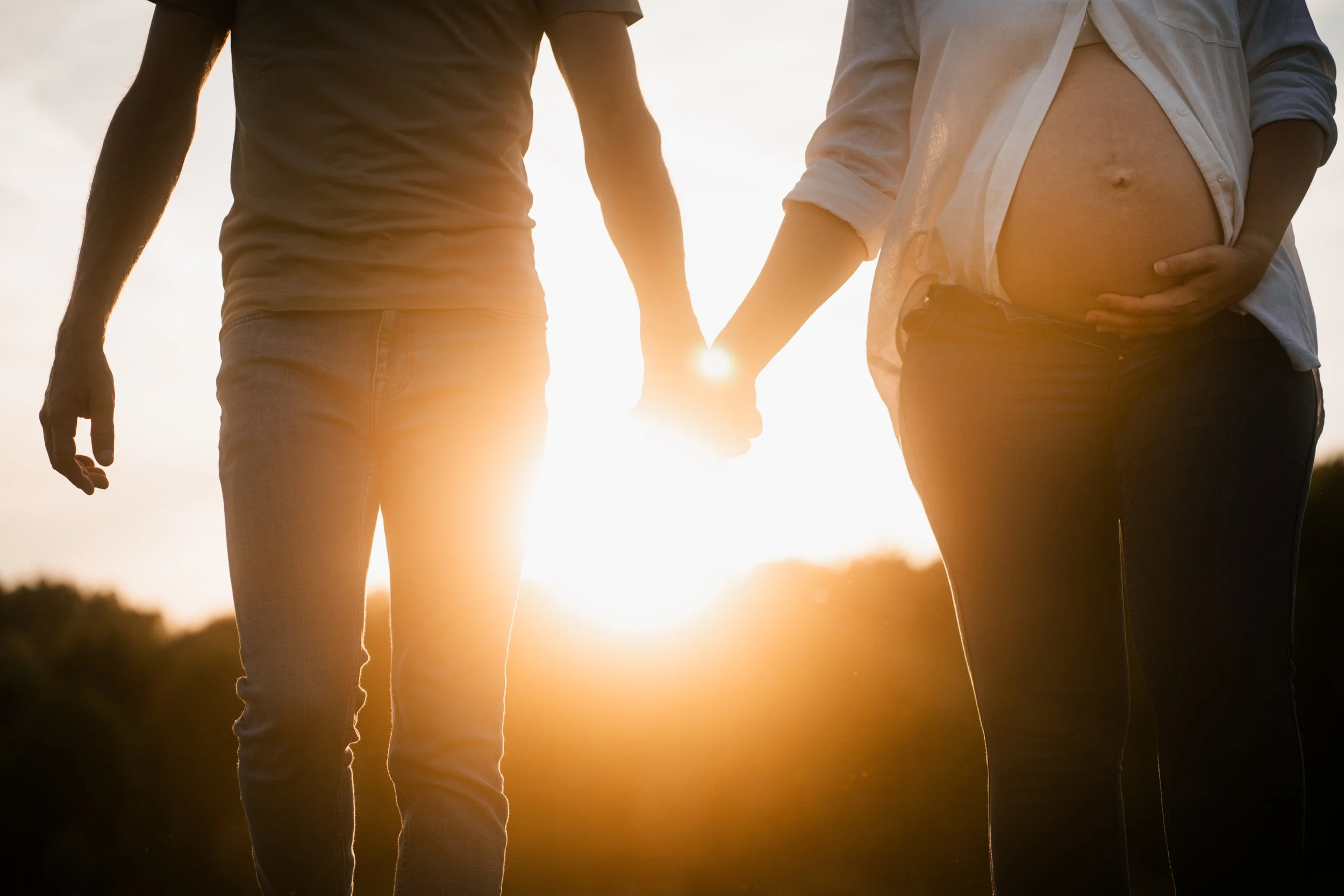 Twee mensen die hand in hand lopen, een van hen is zwanger, tijdens zonsondergang.