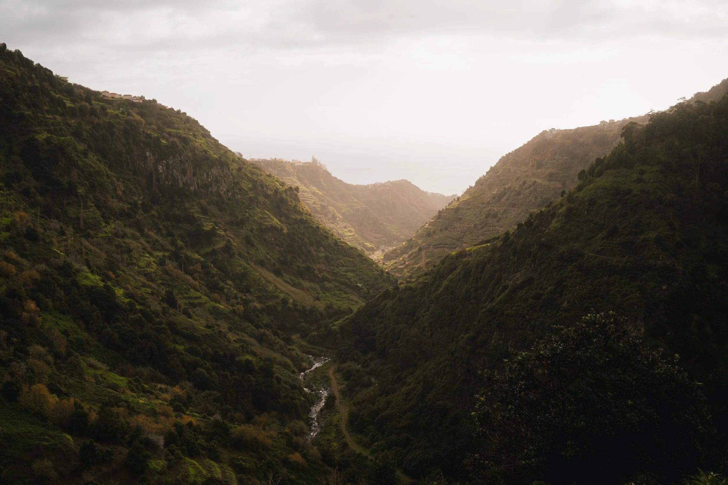 Landschap met groene bergen en een smal riviertje in een vallei, bewolkte hemel