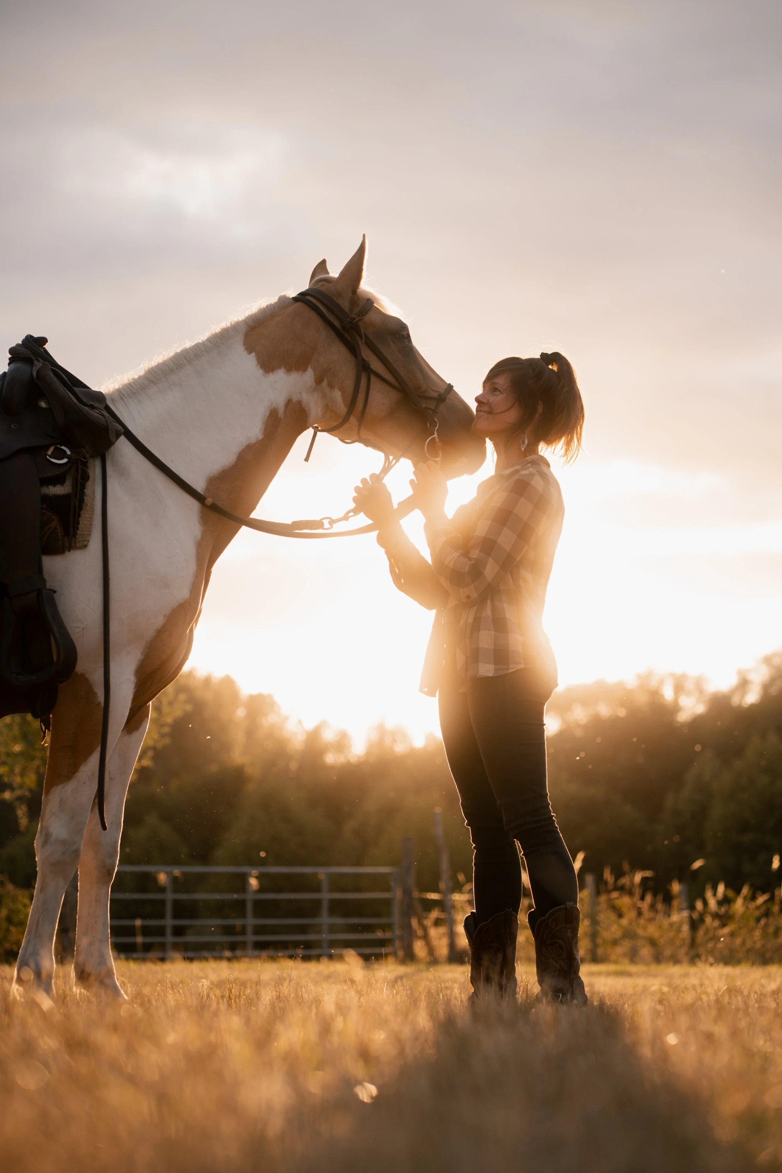Vrouw knuffelt paard tijdens zonsondergang in een veld.
