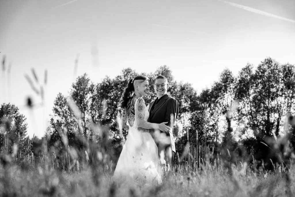 Twee mensen in formele kleding dicht bij elkaar, lachend, in een natuurlijke buitenomgeving met bomen op de achtergrond, zwart-wijn afbeelding.