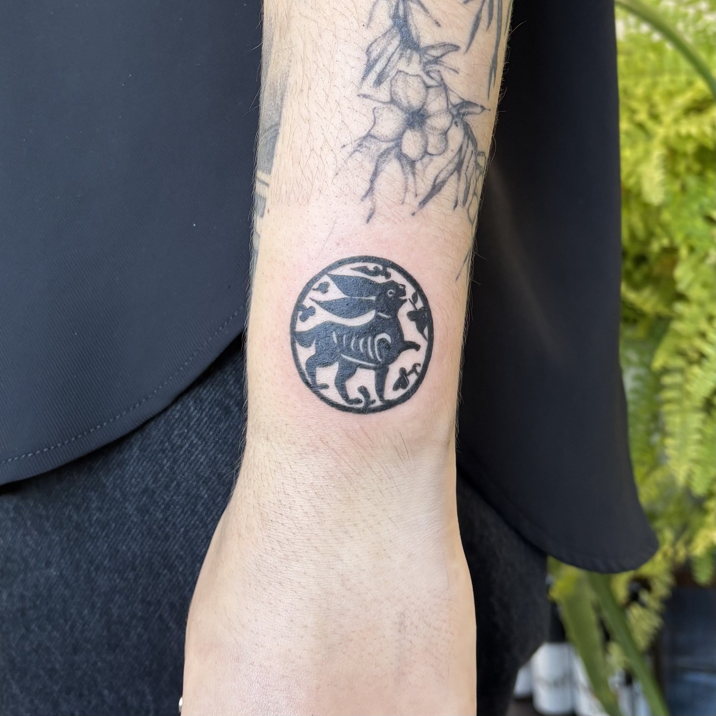 Tattoo of a circular design featuring a winged creature holding an object