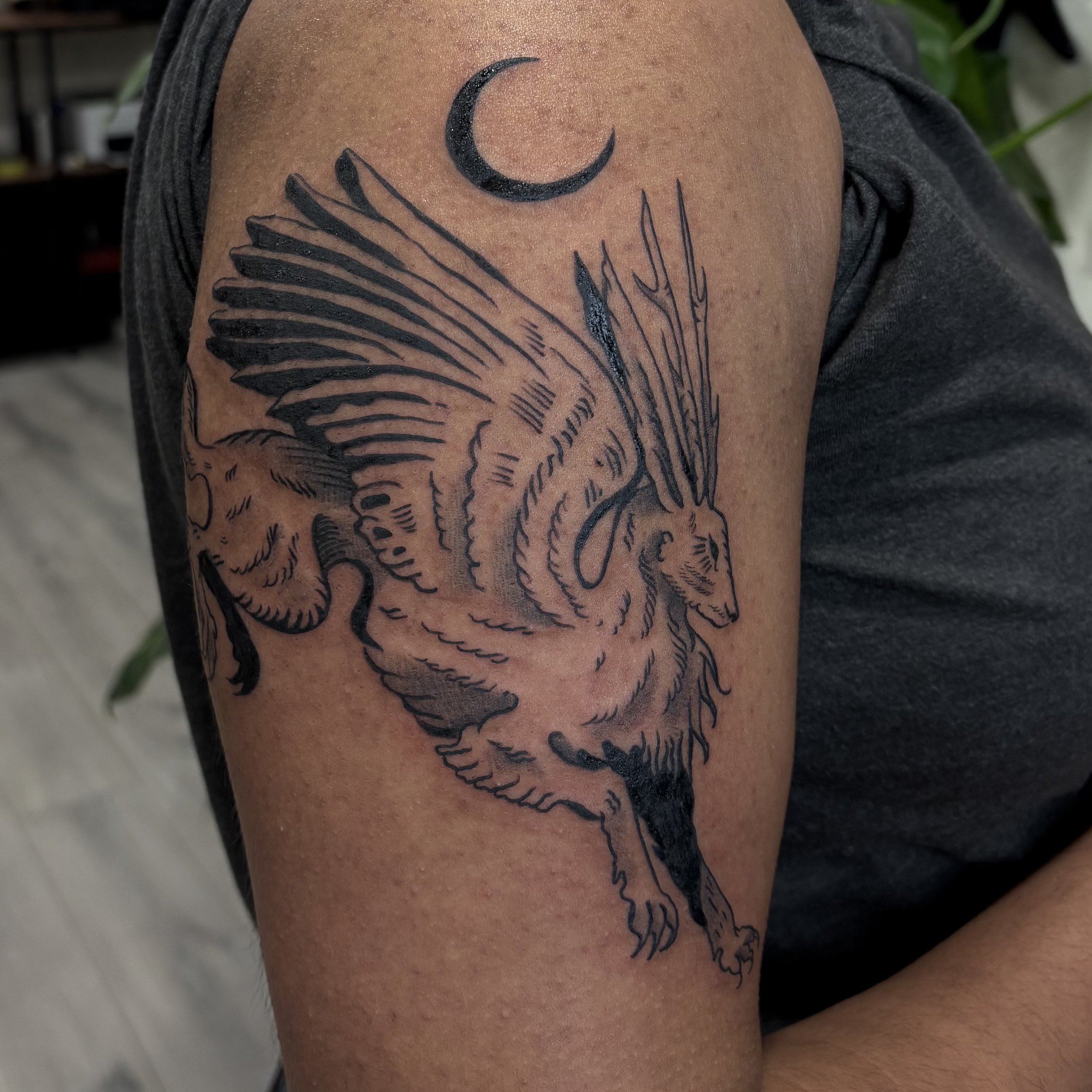 Tattoo of a phoenix bird with large wings on a person's upper arm, with a crescent moon above it.