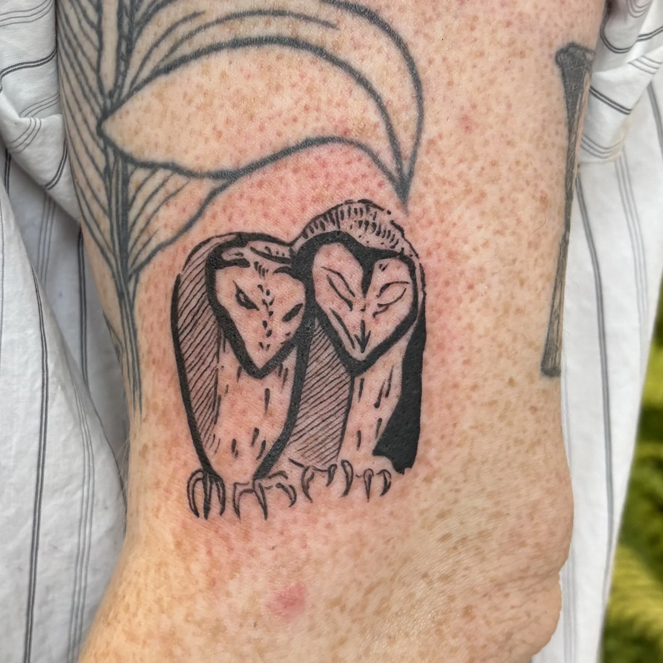 A fresh black outline tattoo of two stylized mice with closed eyes, positioned side by side, on a person's upper arm.
