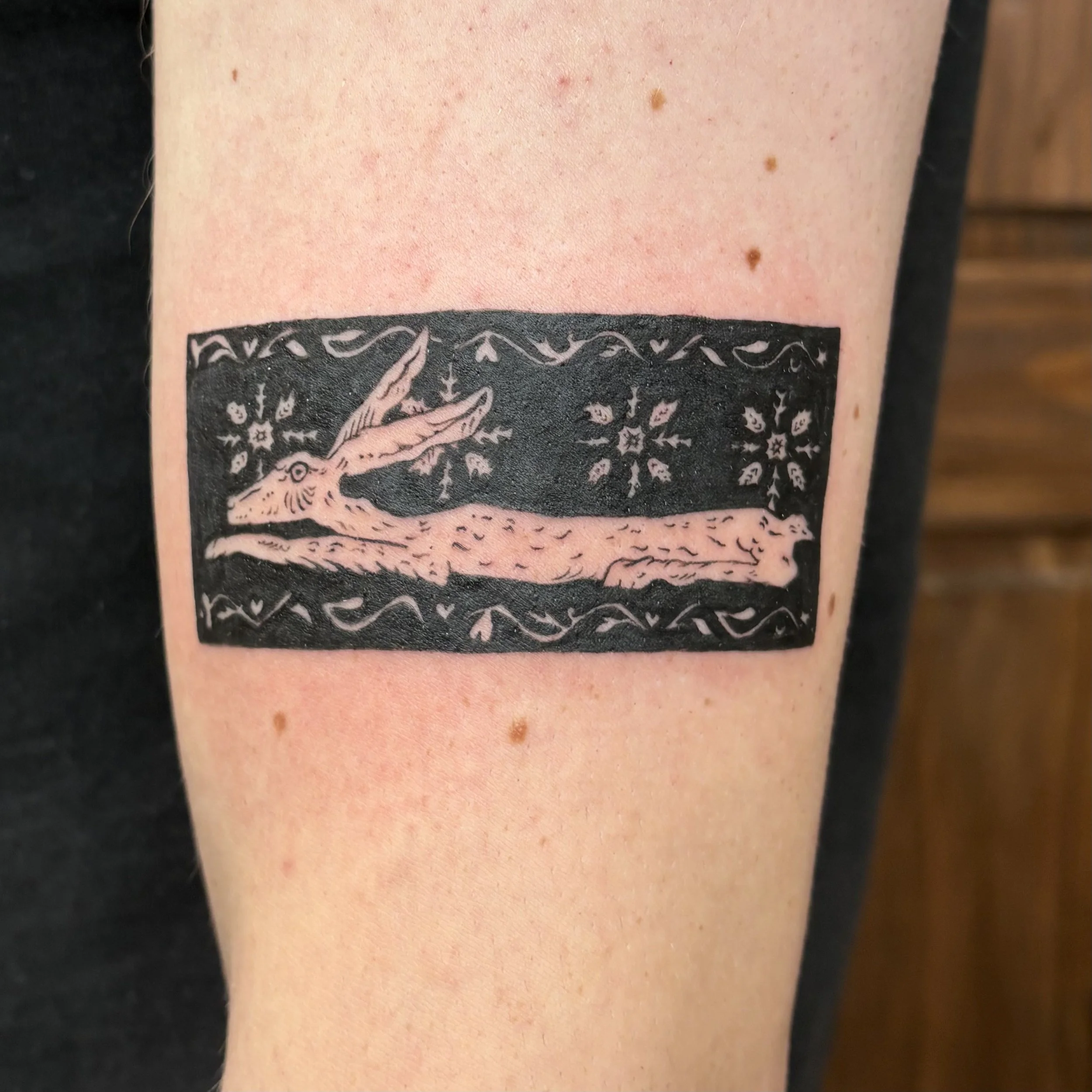 A tattoo of a stylized rabbit in black and pink ink on a person's arm surrounded by decorative floral patterns.