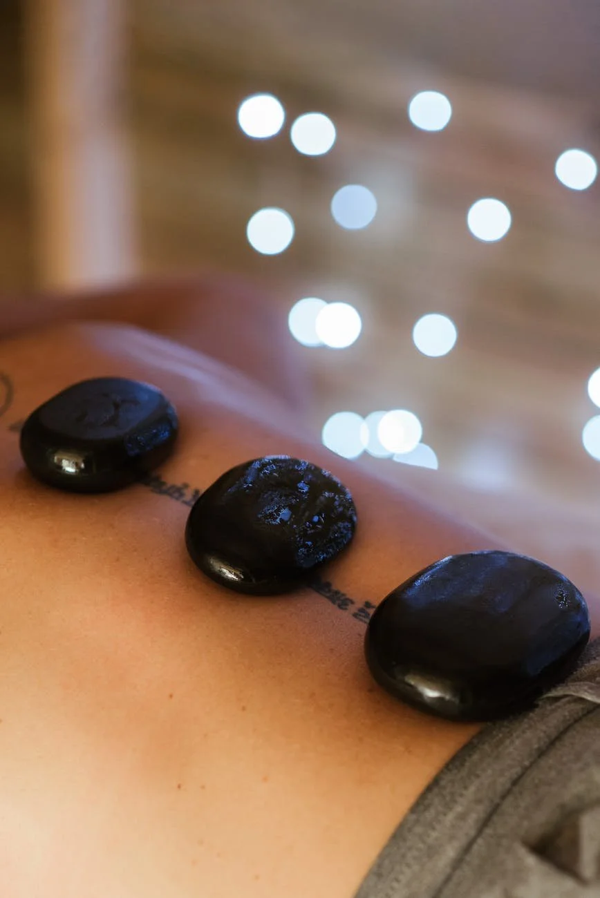 Hot stones placed on a person's back during a massage, with blurred string lights in the background.