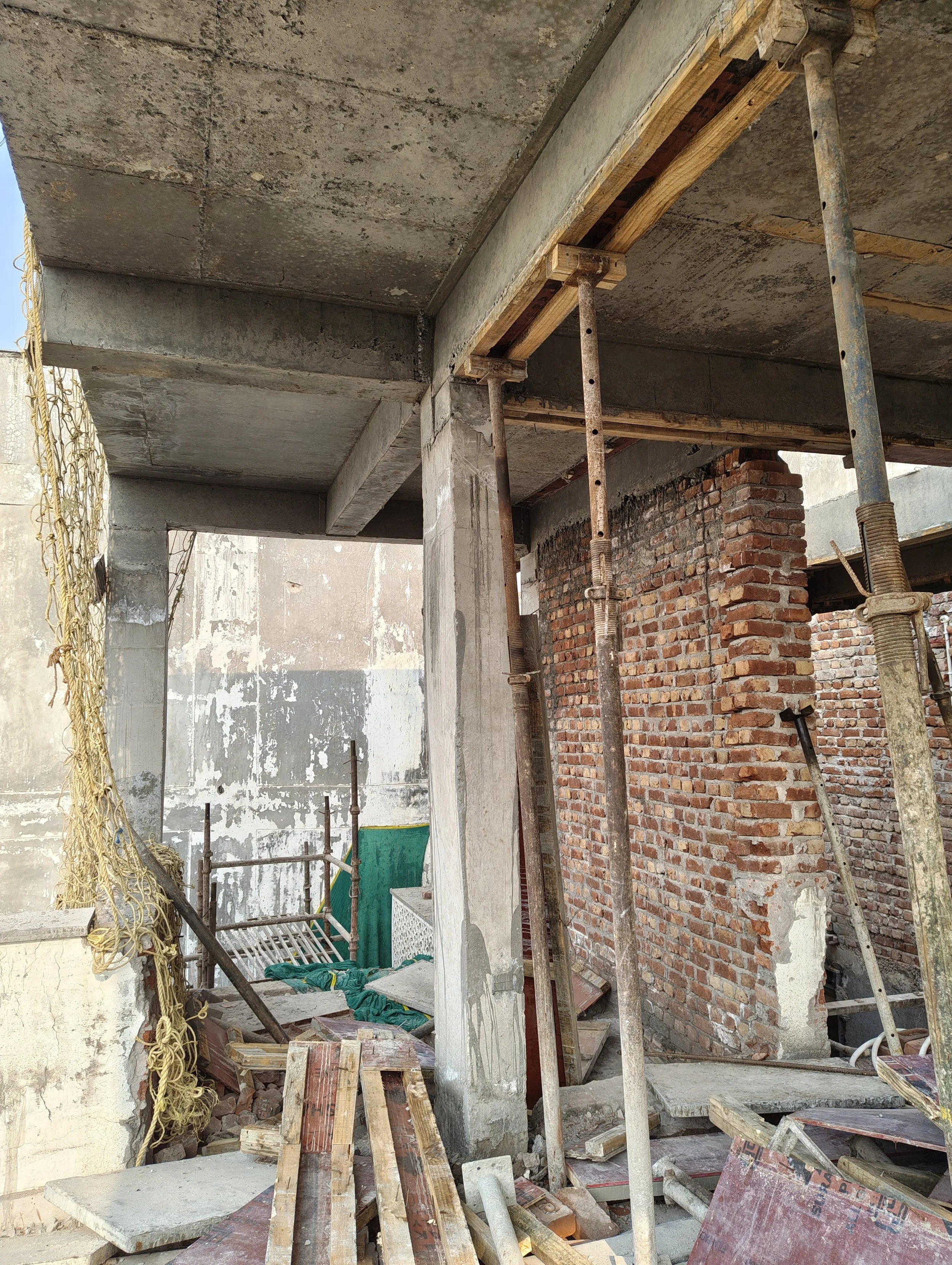 Construction site with concrete pillars, brick wall, scaffolding, and building materials.