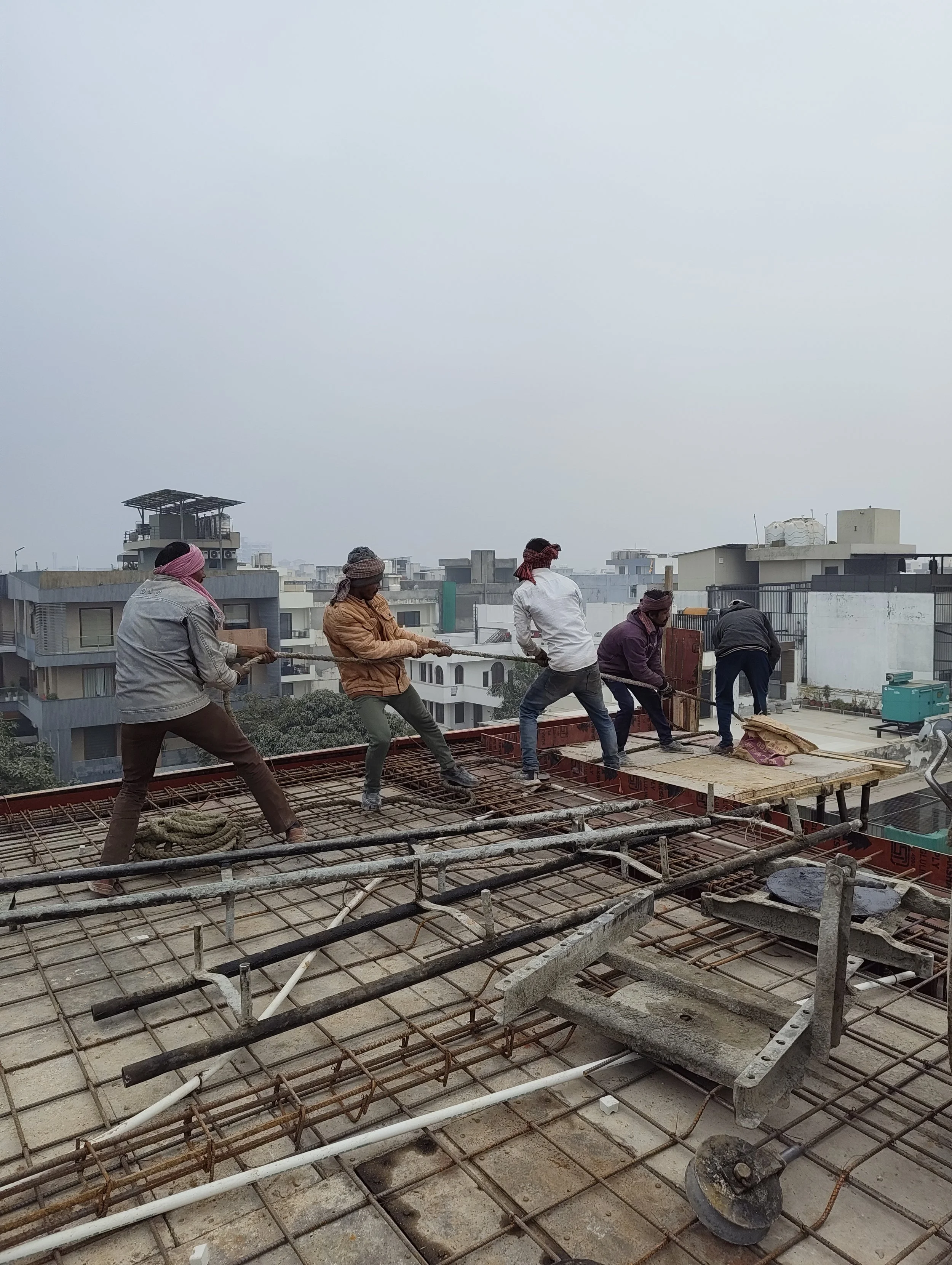 Construction workers pulling a rope on a building rooftop with cityscape in the background.