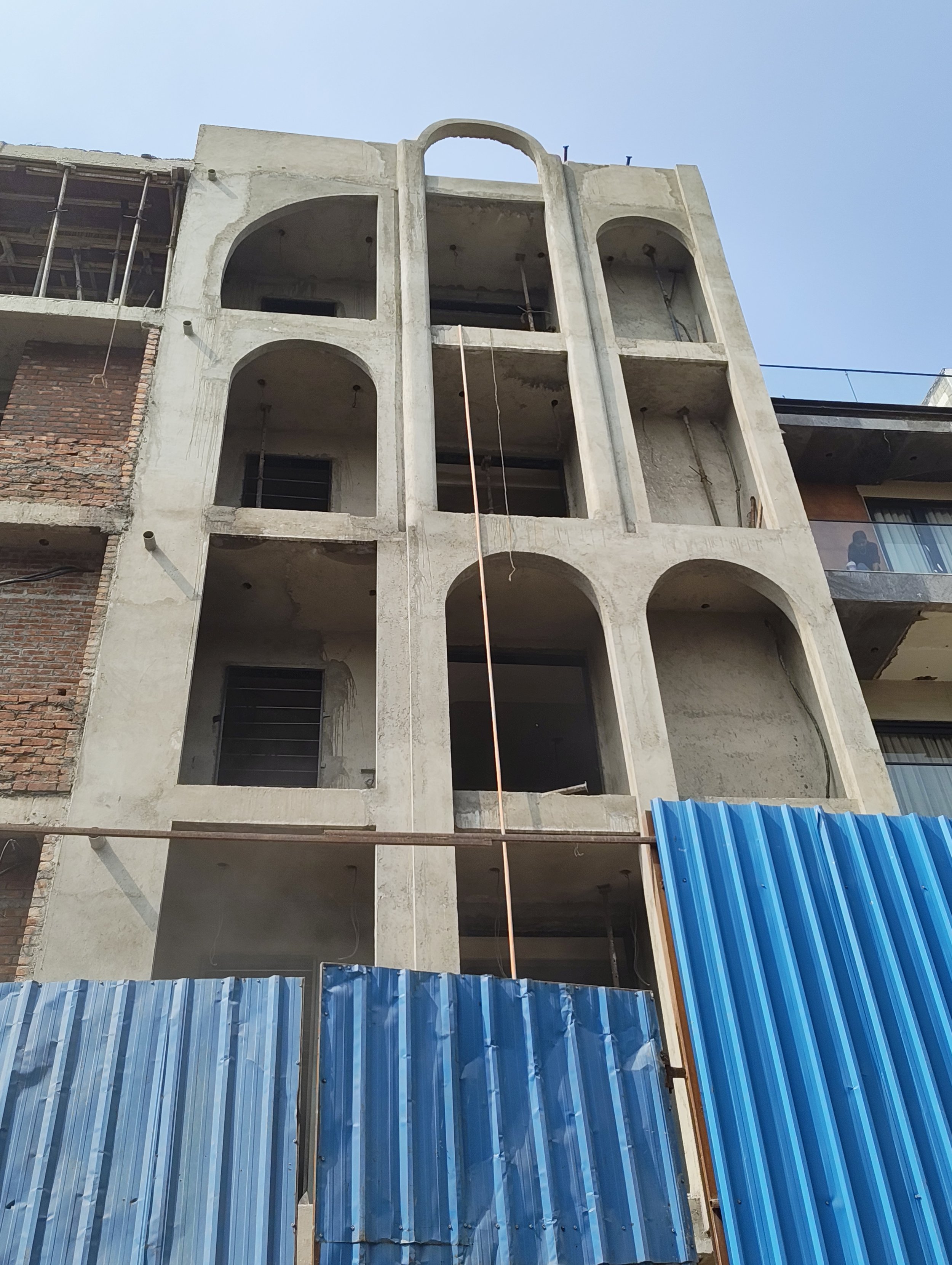 A multi-story building under construction with exposed brick walls and concrete floors, laundry hanging outside on one level, and construction equipment at the base.