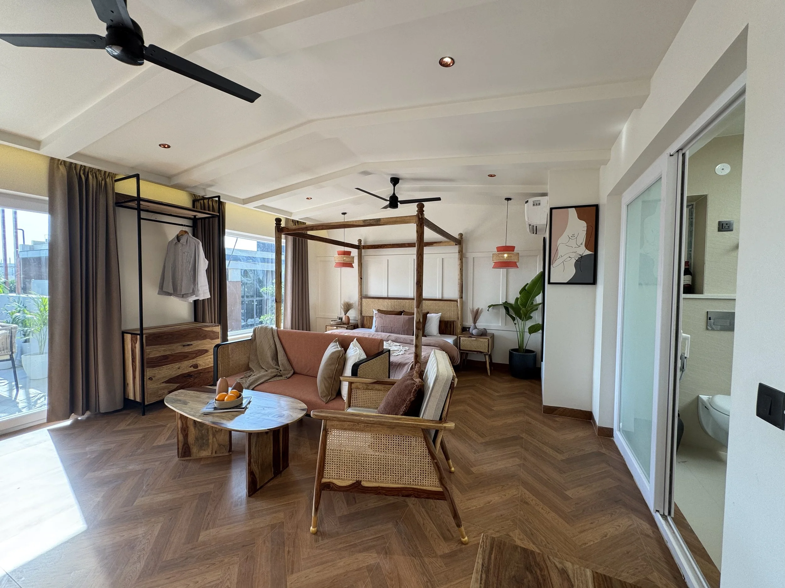 A modern bedroom with wooden flooring, a canopy bed, a sofa, and art decor, with sliding glass doors leading to an outdoor space.