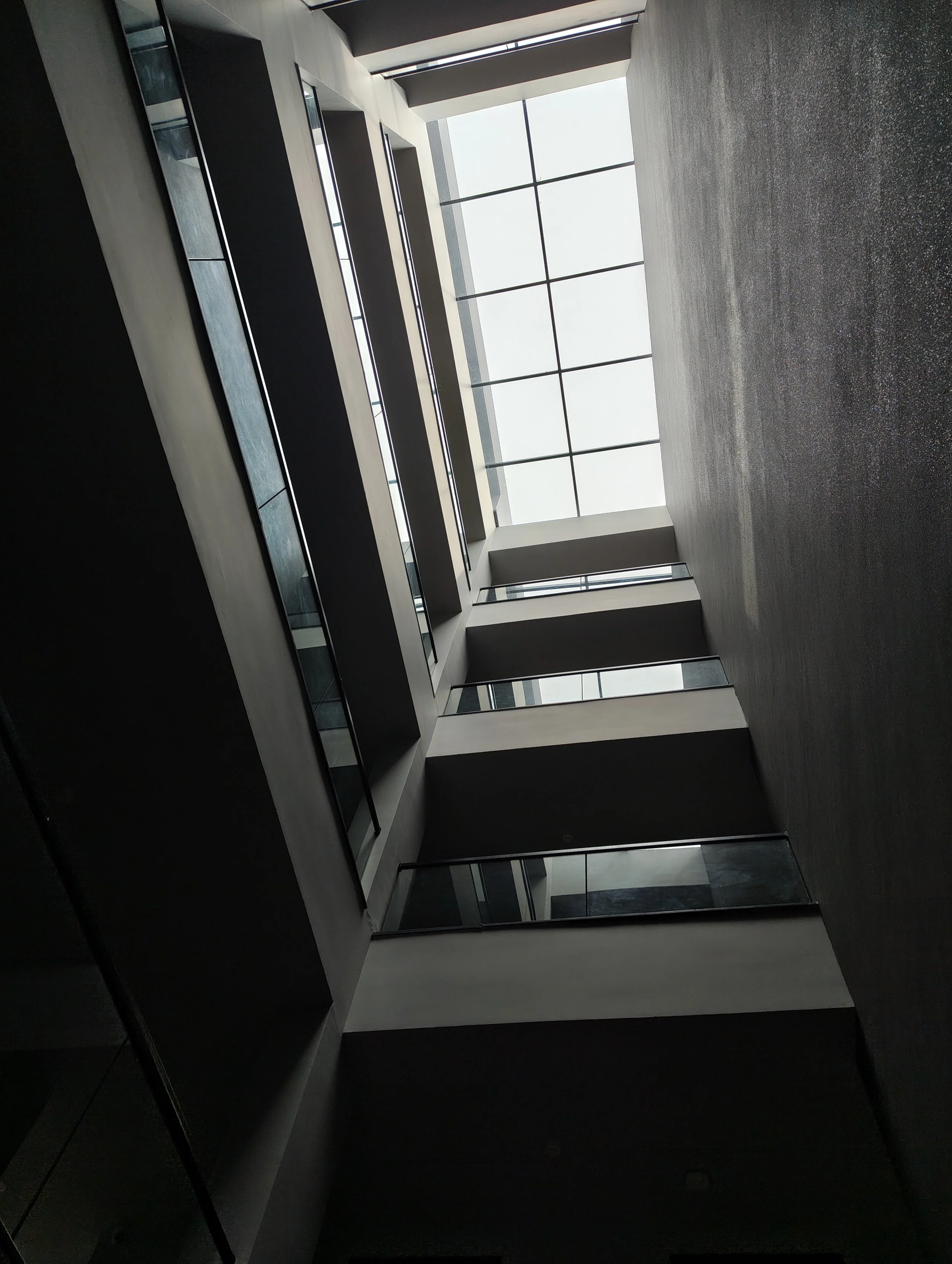 Interior view of a modern multi-story building with a central open courtyard and large windows at the top letting in natural light.