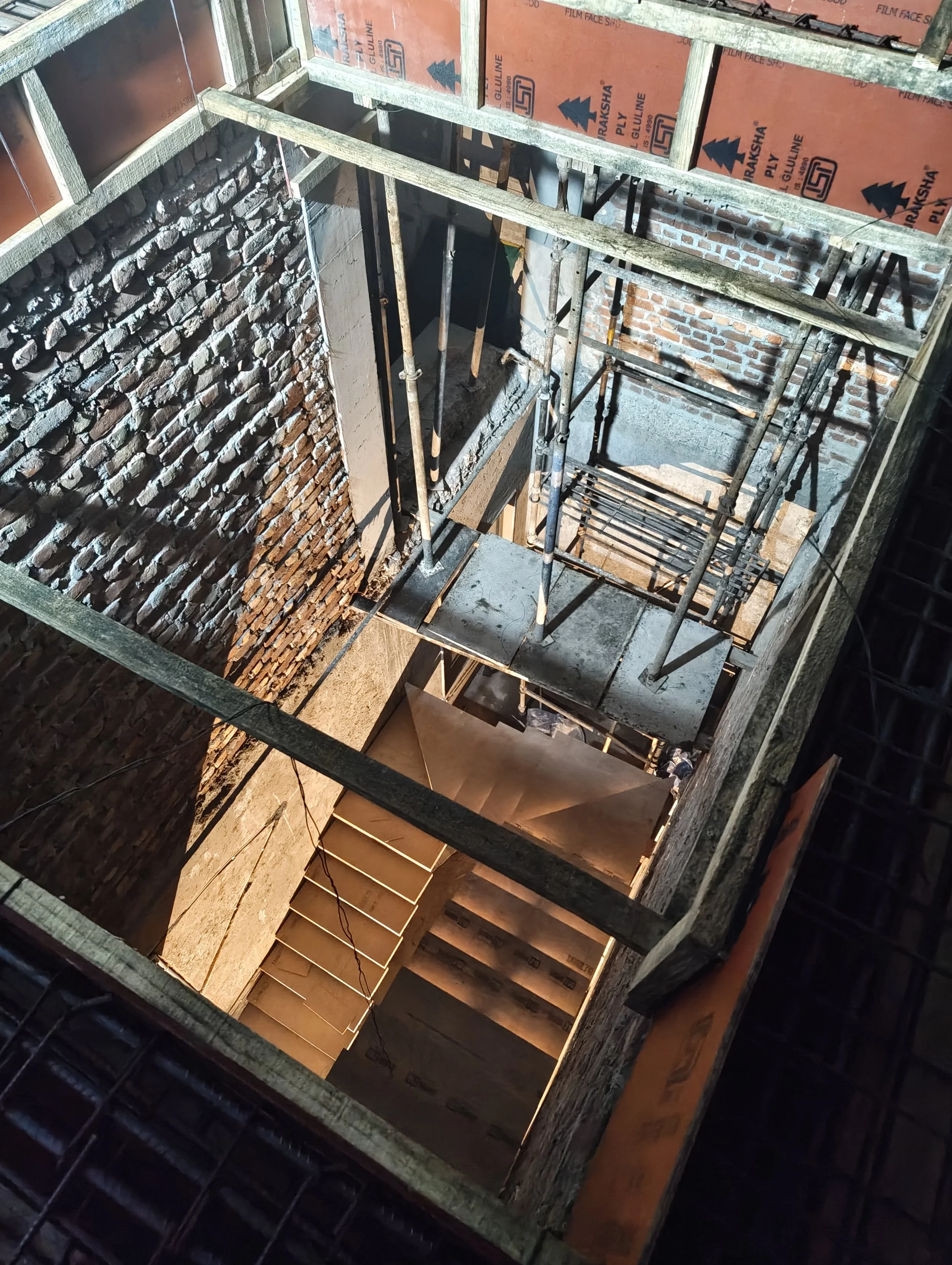 View of a construction site showing a multi-story building under construction with brick walls, scaffolding, and wooden stairs.