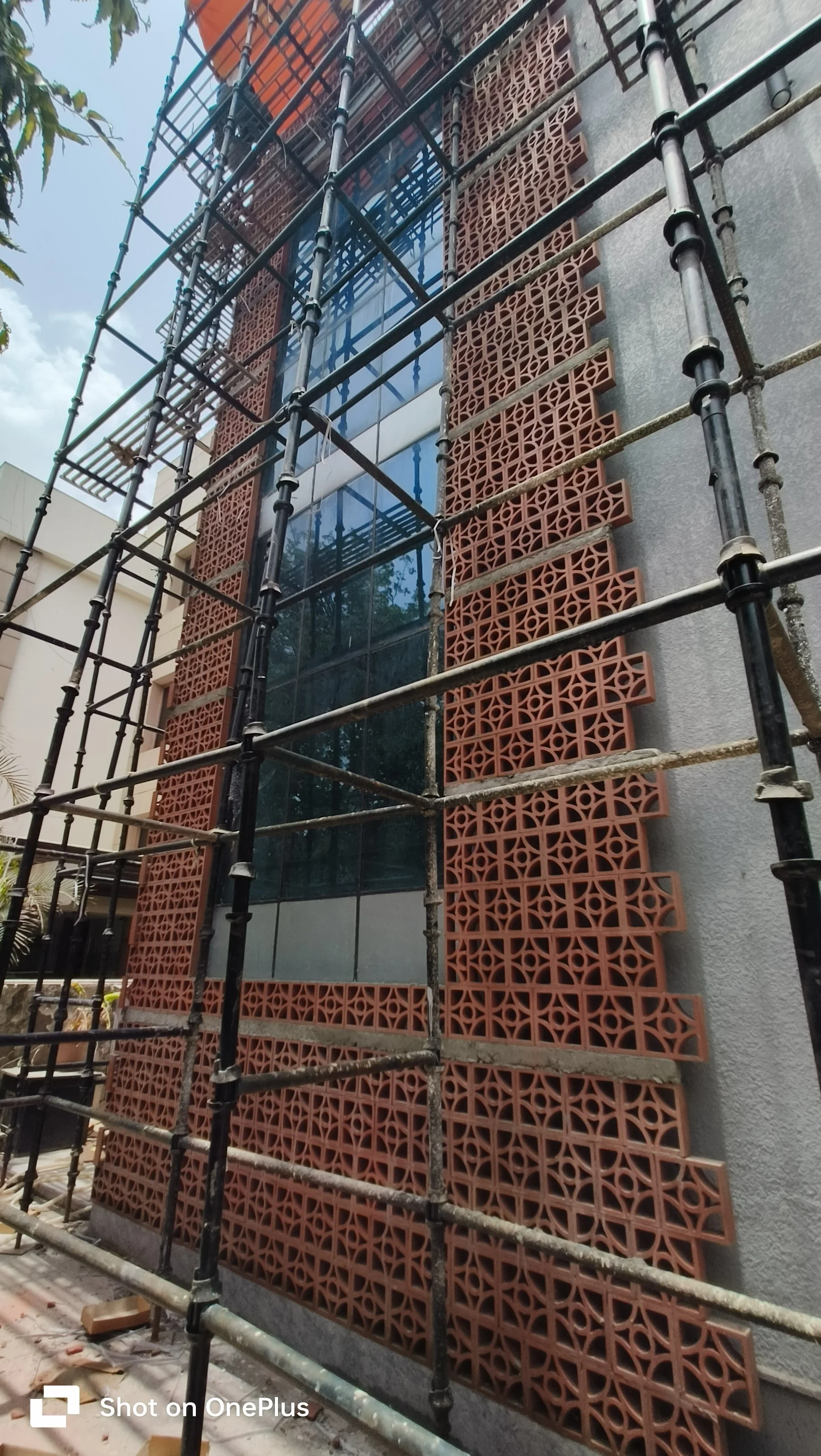 Construction scaffolding surrounds a building with decorative brick wall panels and large glass windows.