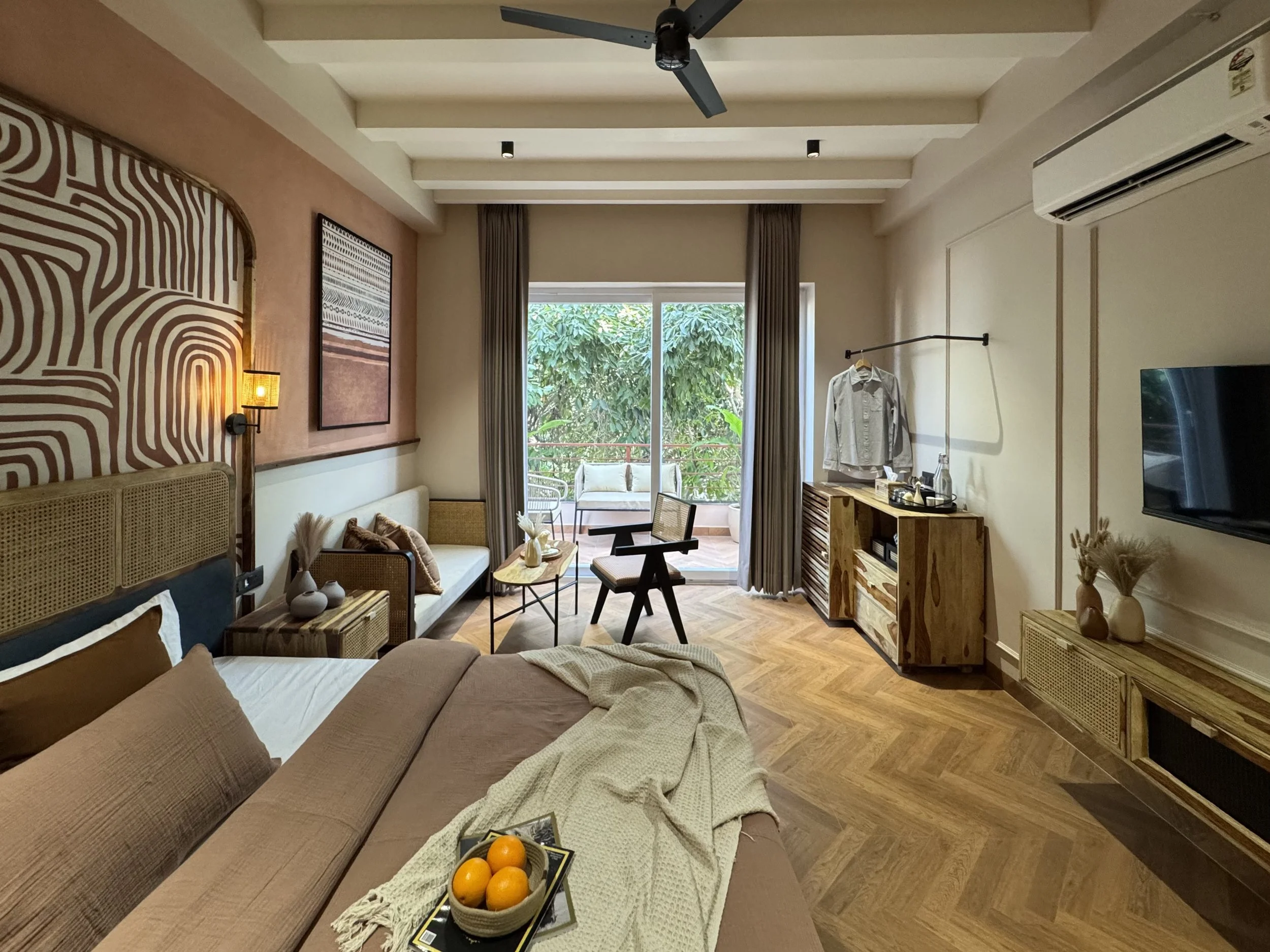 A cozy hotel room with a king-sized bed, sitting area, balcony with outdoor furniture, wooden flooring, and modern decor.