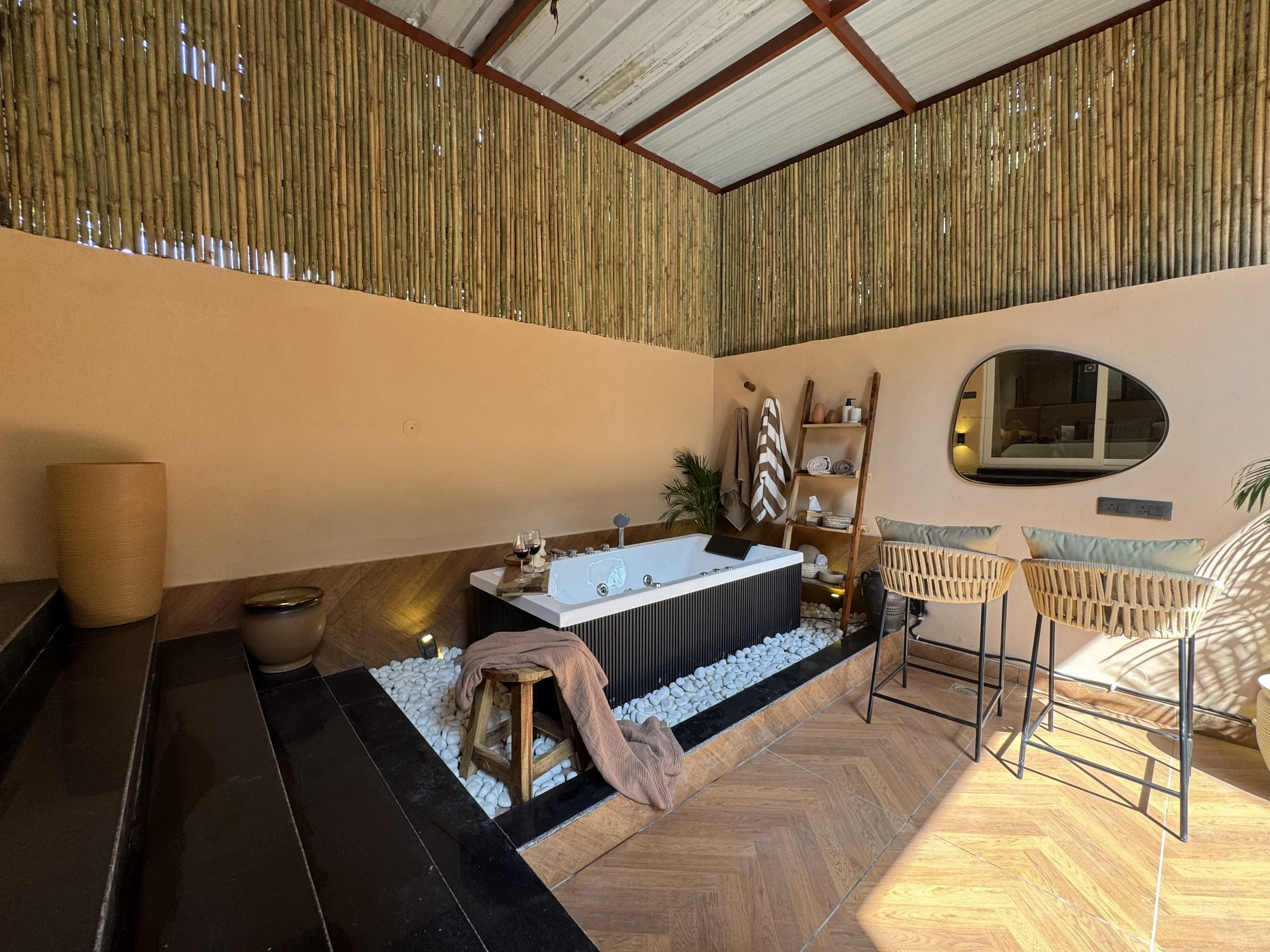 A cozy indoor space with a bathtub, two bar stools, and natural decor elements including bamboo accents and white stones, creating a spa-like atmosphere.