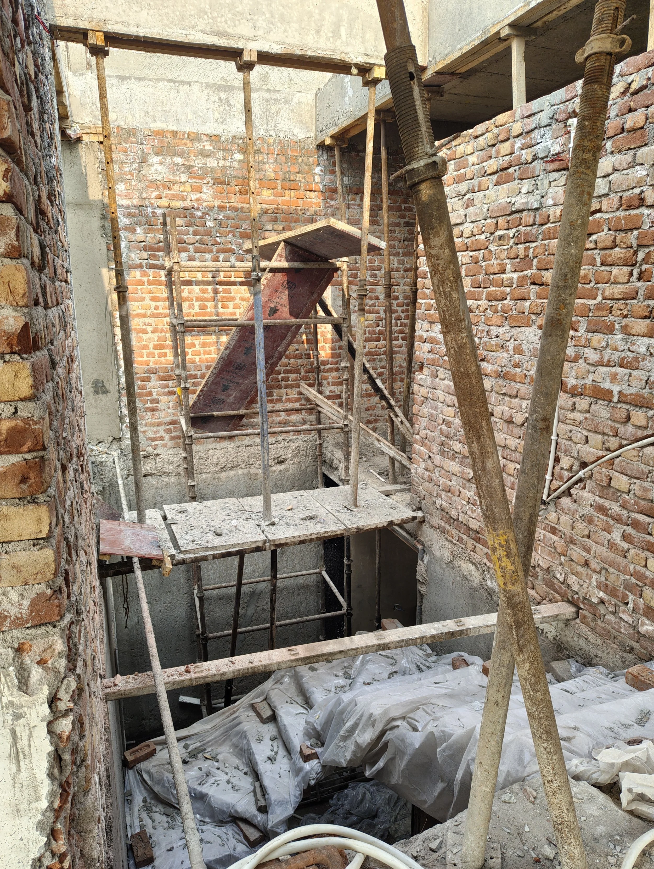 Construction site with scaffolding and brick walls, showing an unfinished interior space.