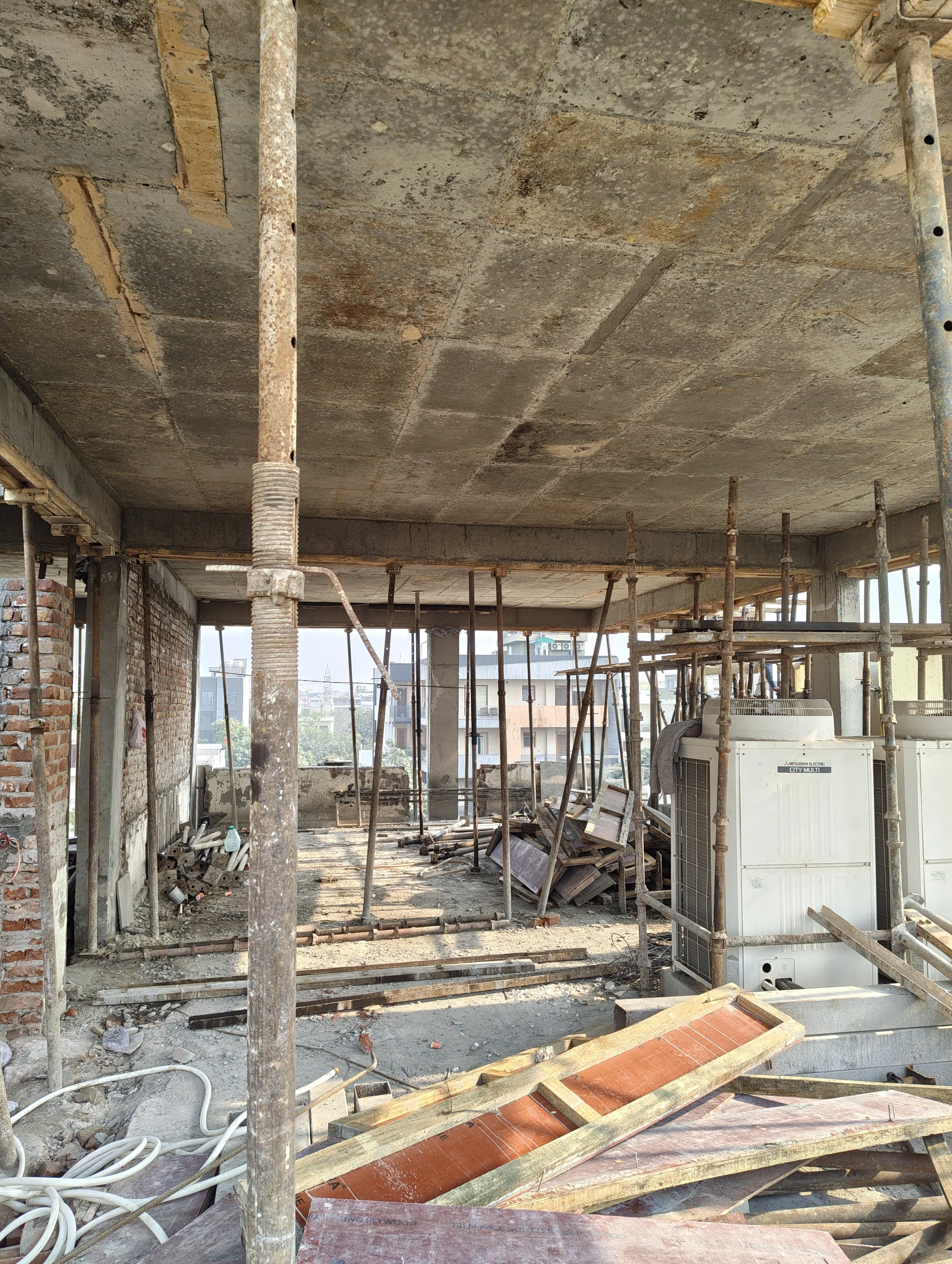 Construction site with scaffolding, concrete ceiling, and tools, overlooking city buildings.