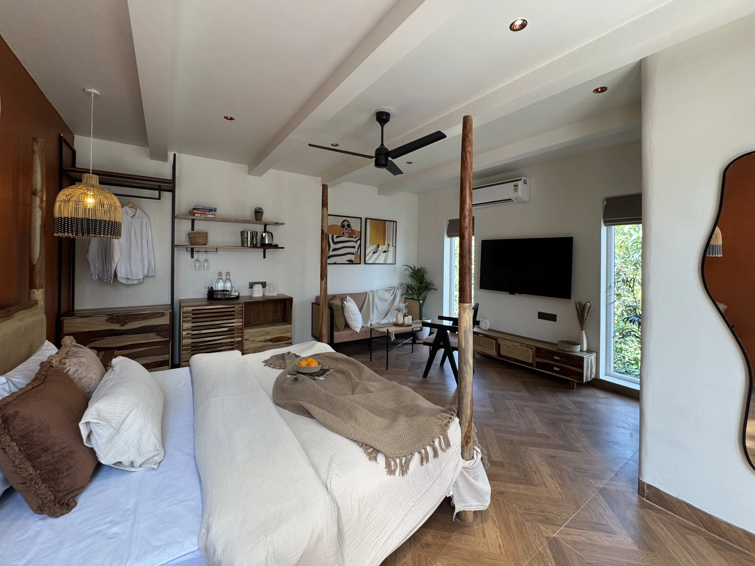 Modern living room with a king-sized bed, wooden decor, wall art, a flat-screen TV, and balcony with greenery.