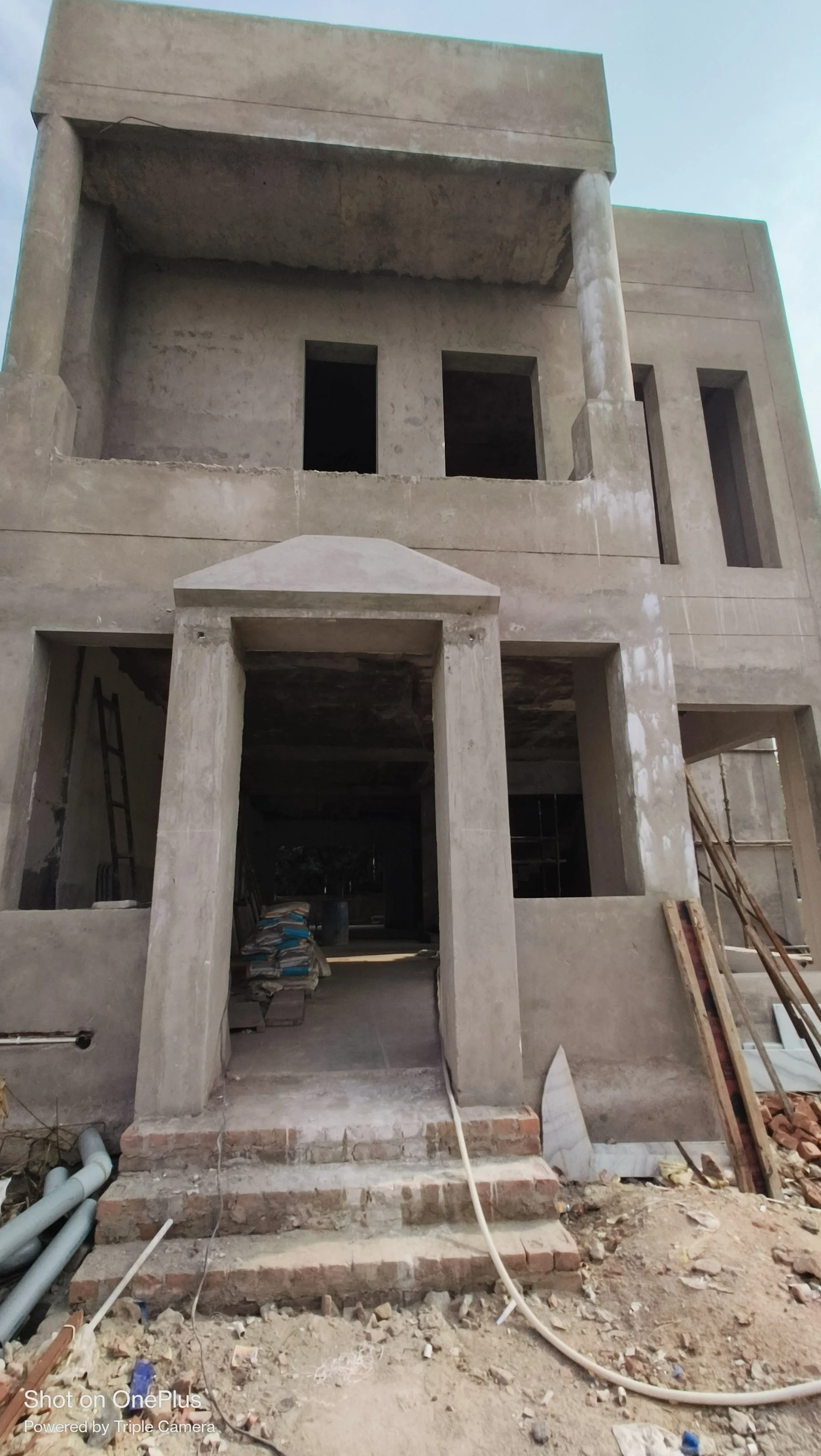 Under construction multi-story building made of concrete with scaffolding and construction materials around the entrance.