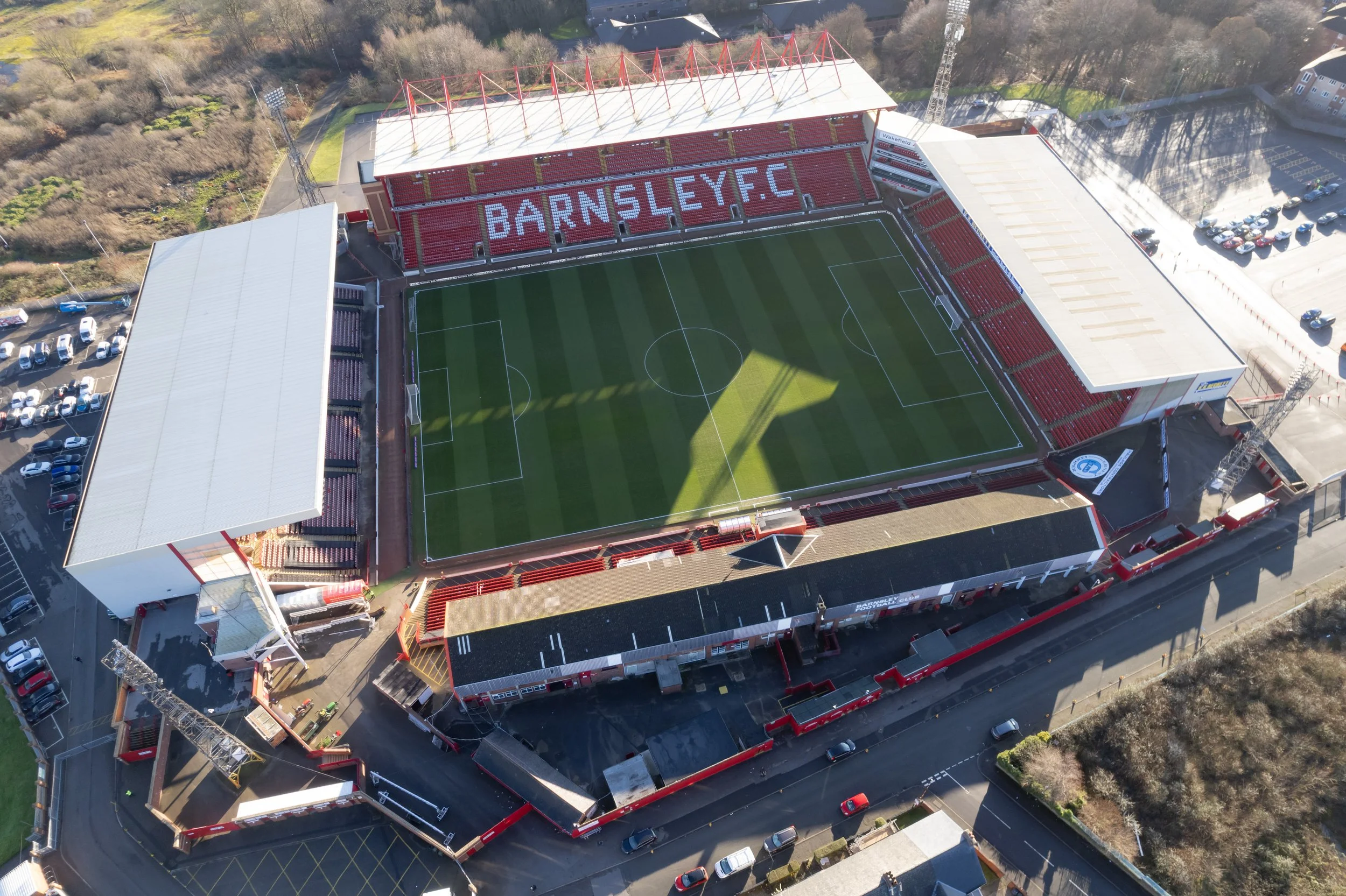 An aerial view of Barnsley Football Club stadium with a green football field, red seating, and surrounding structures.