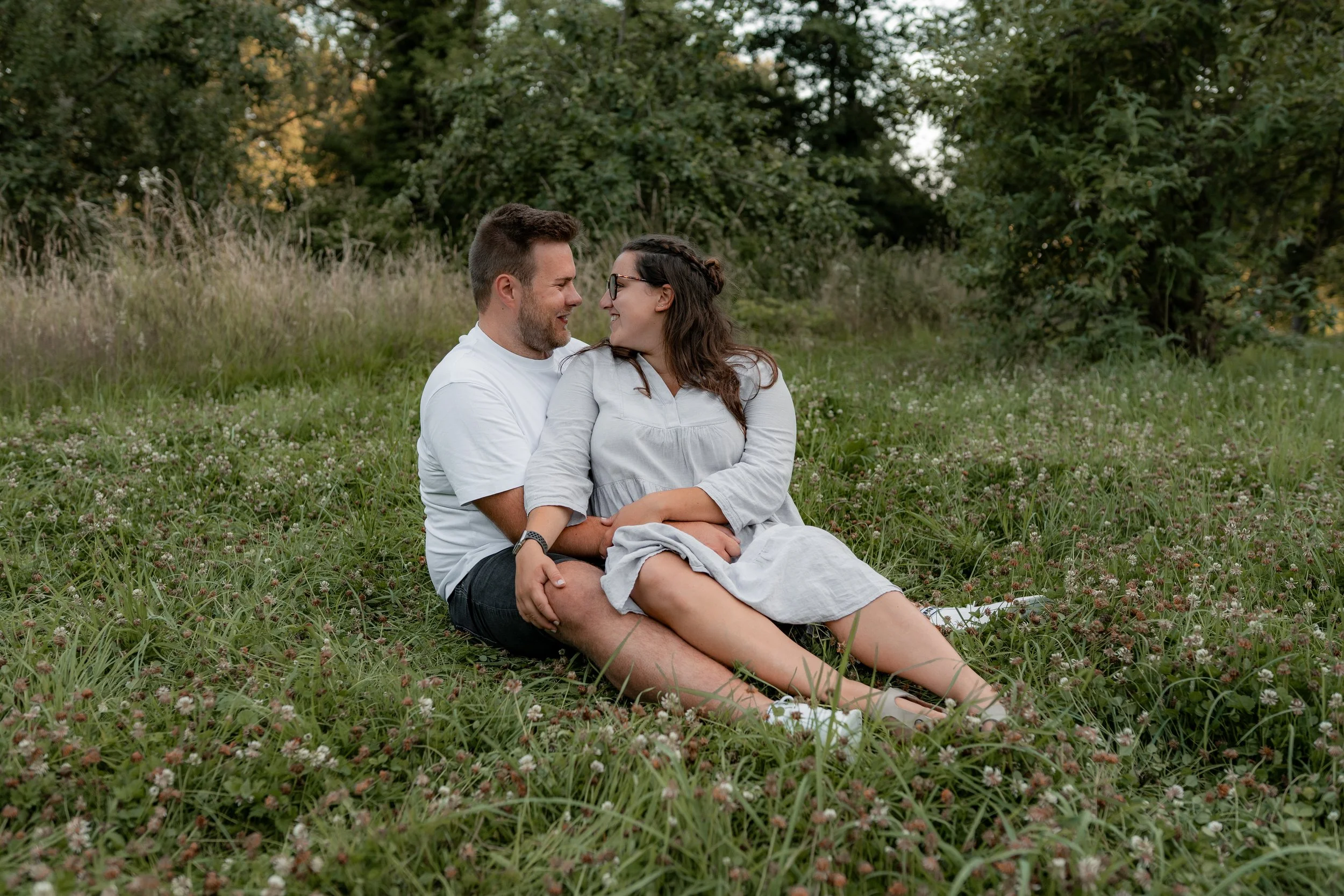 Ein Paar sitzt im Grünen auf einer Wiese und schaut sich liebevoll an.
