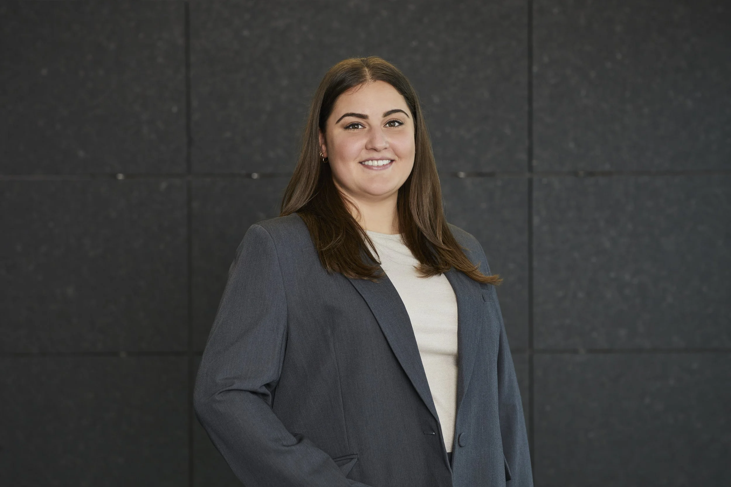 Eine lächelnde Frau in dunklem Anzug vor einer schwarzen Steinwand. REM TRANSACTION GmbH