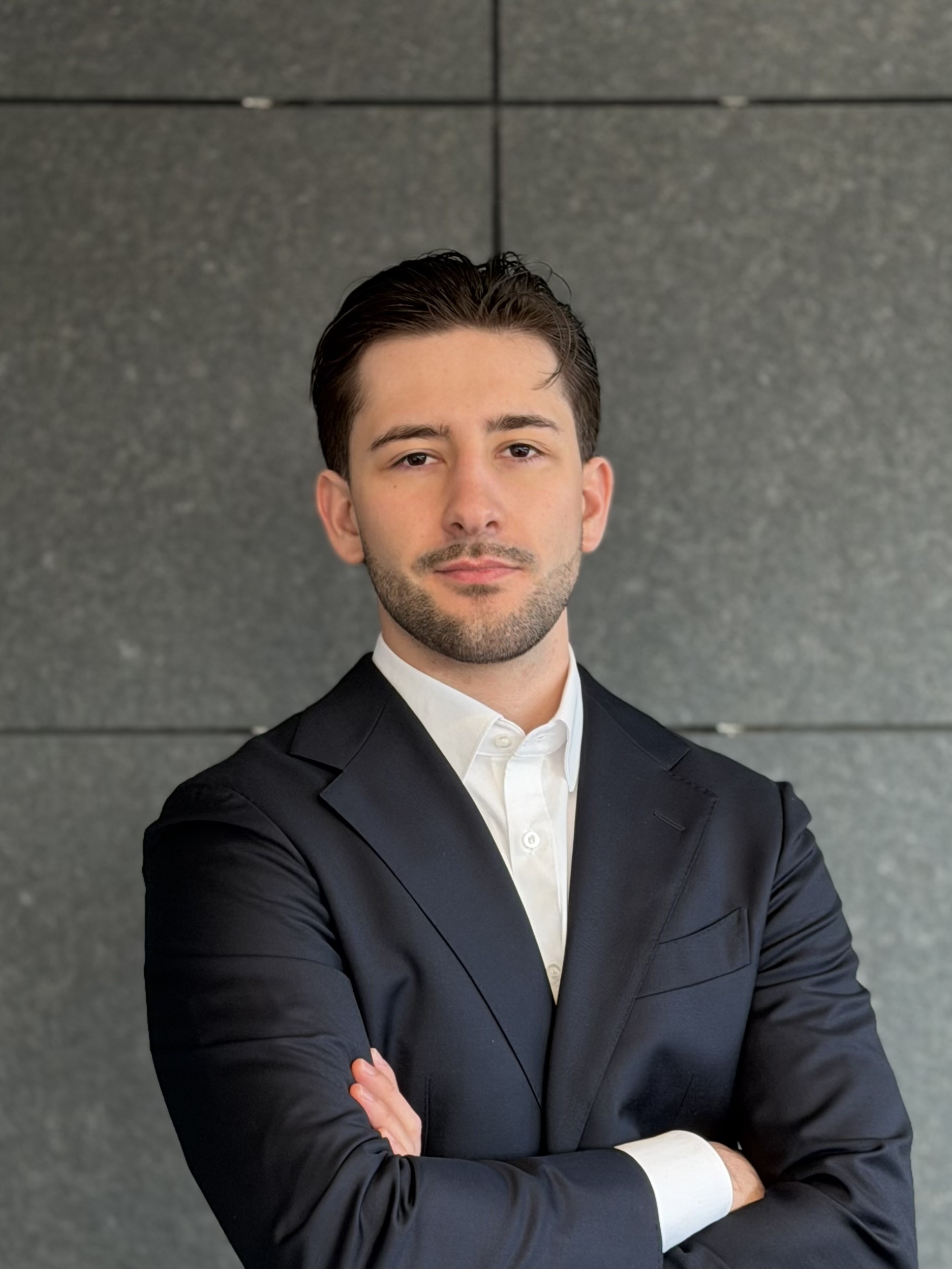 Junge Mann mit Brille, lächelnd, trägt ein weißes Hemd mit Streifen, steht vor einer schwarzen Wand. REM TRANSACTION GmbH