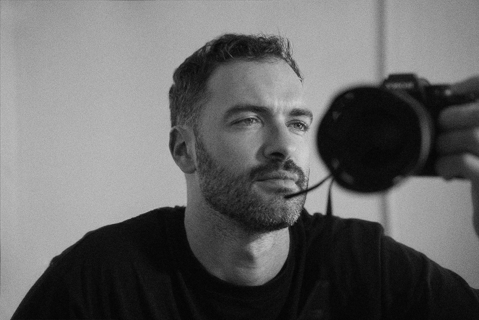 Un homme avec une barbe regarde un appareil photo, image en noir et blanc.