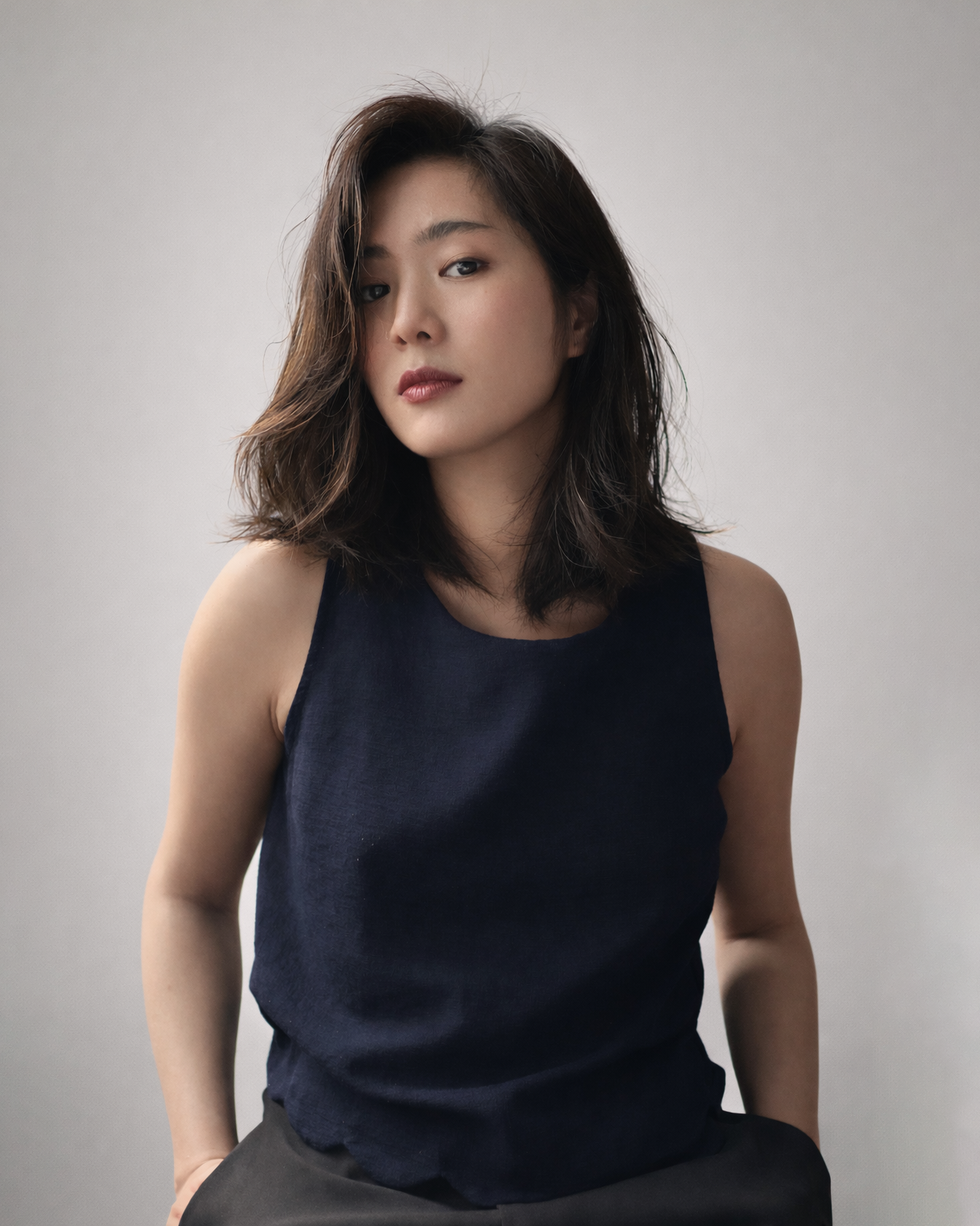 A woman with shoulder-length dark hair wearing a sleeveless navy blue top against a plain gray background.