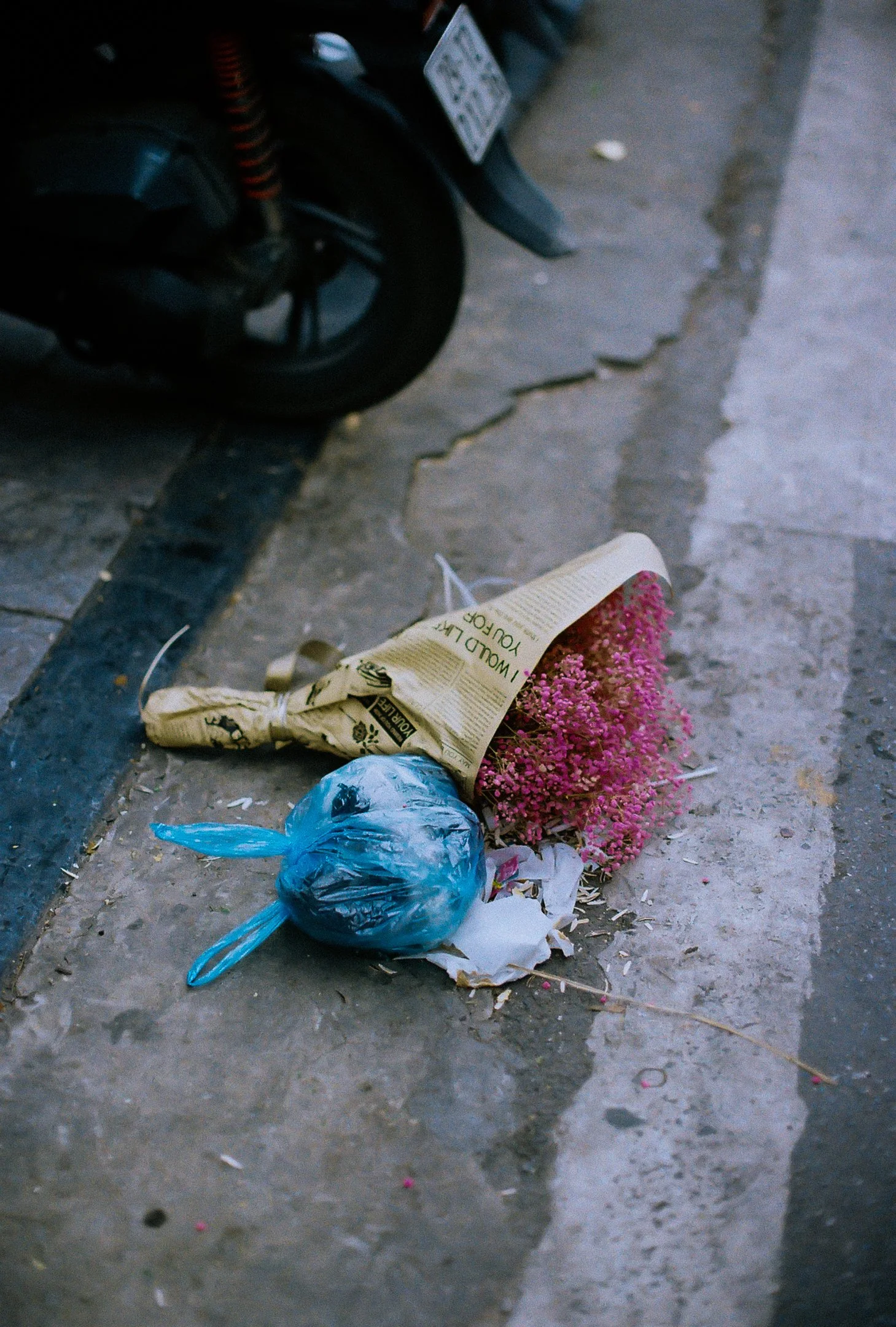 Des déchets abandonnés sur le trottoir, dont un bouquet de fleurs enveloppé dans du papier et un sac en plastique bleu.