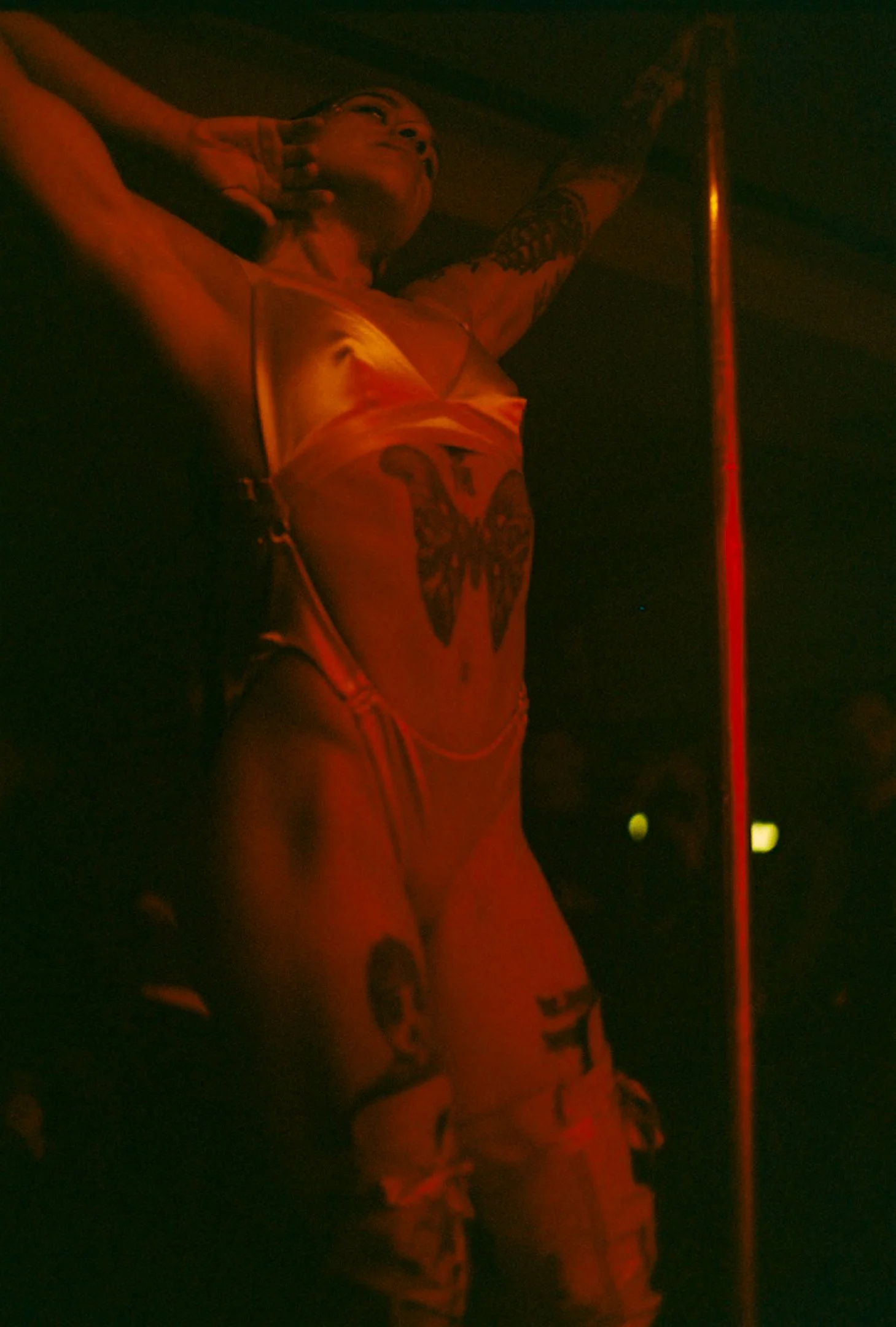 Une femme posant avec un bâton de pole dance dans une ambiance sombre avec un éclairage rouge.