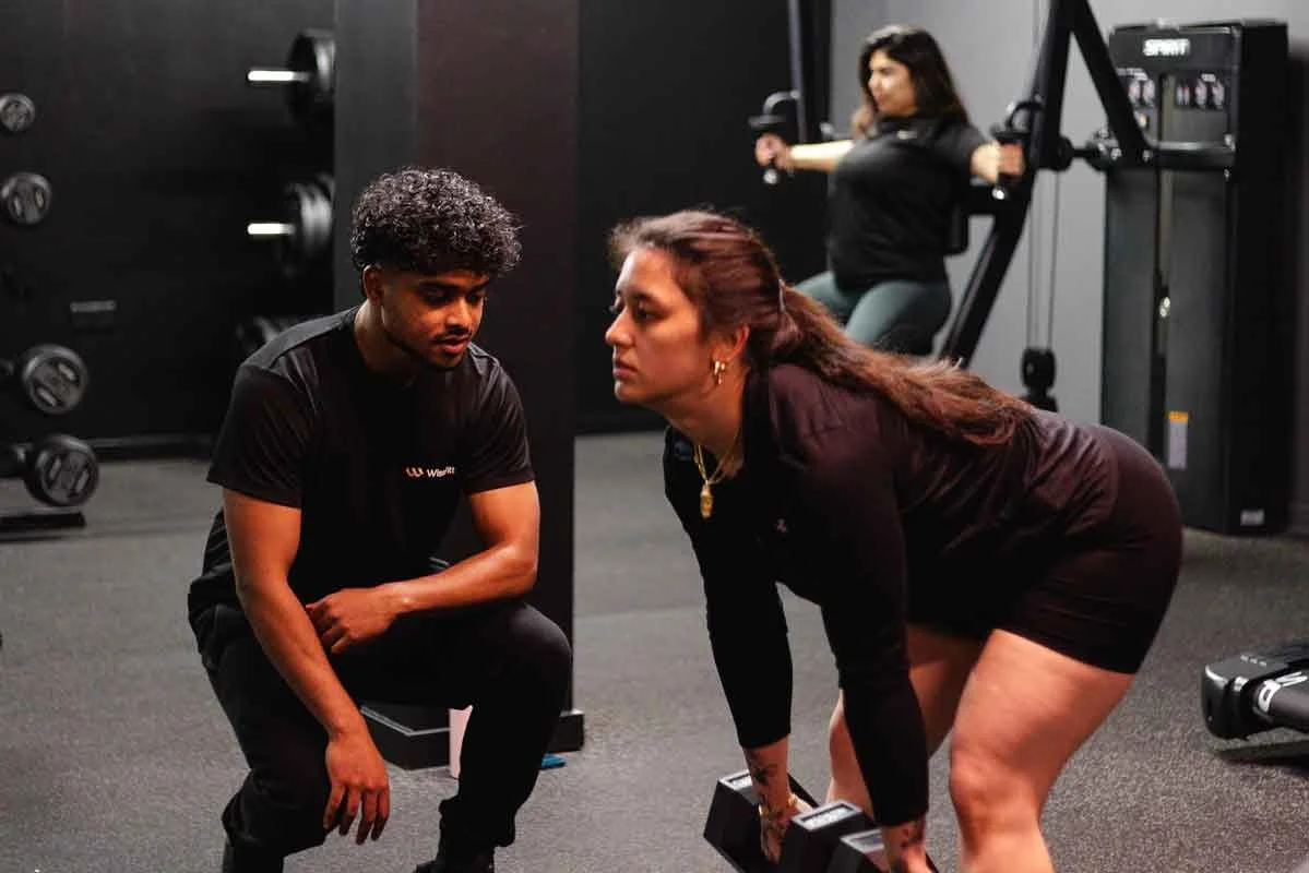 A personal training session where a PT is expertly watching a user lift weights at WiseFitt Gym in Fulham