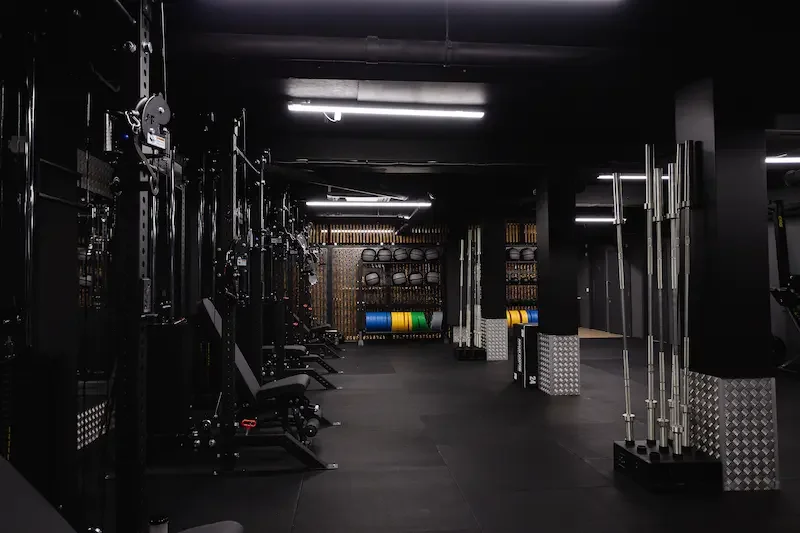Empty gym with various workout equipment including barbells, medicine balls, and colorful weight plates organized on racks.