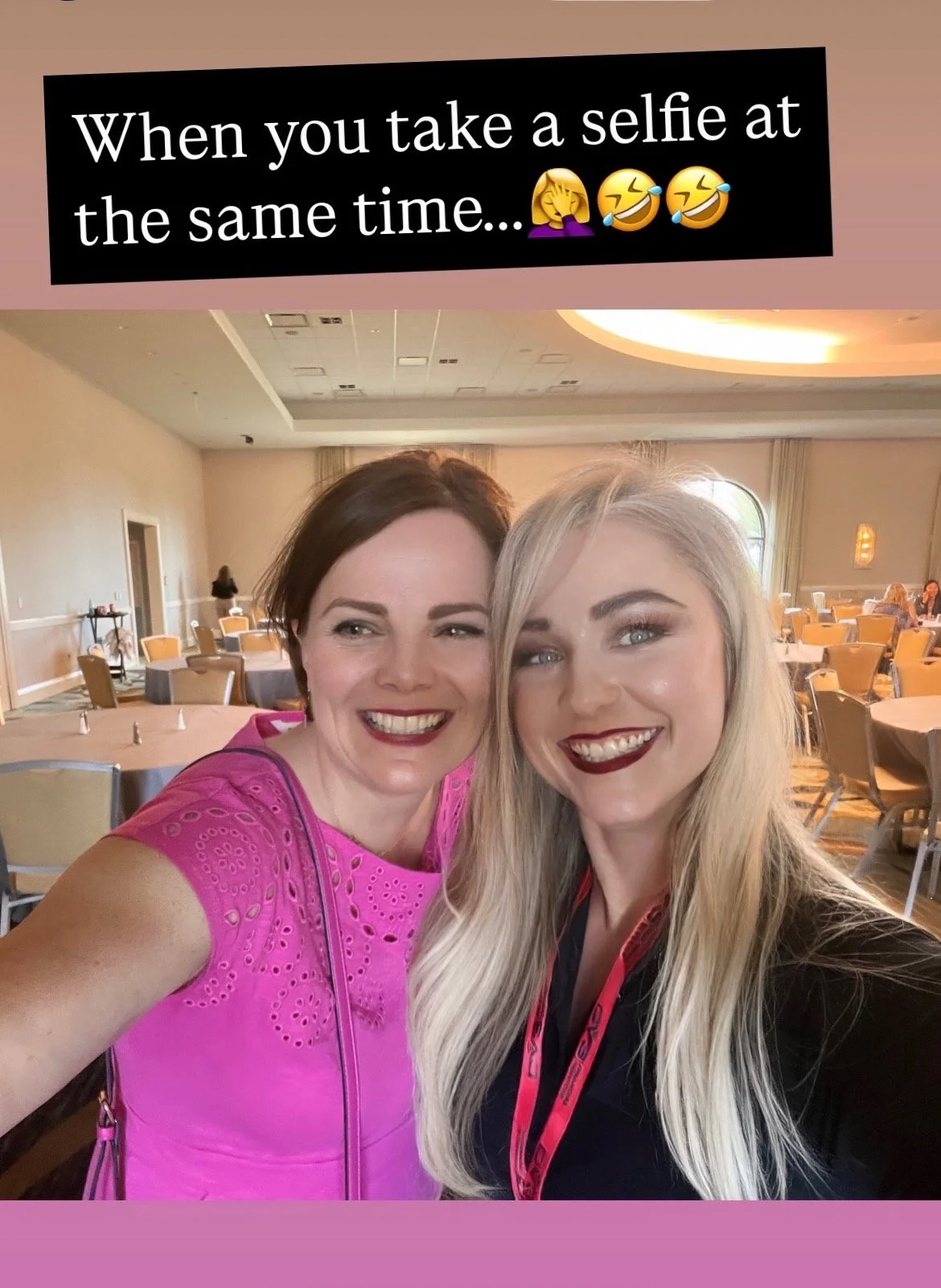 Two women smiling for a selfie at an indoor event space, with tables and chairs in the background.