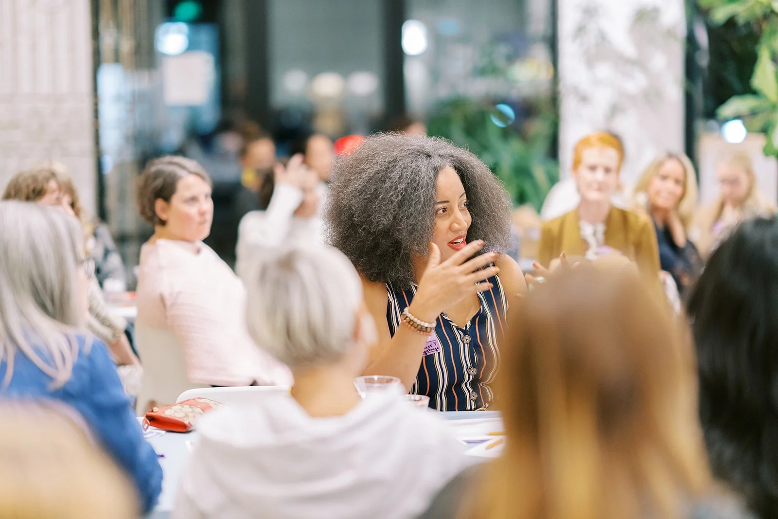 A group of women seated at a meeting or conference, engaging in discussion, with one woman in the center speaking.