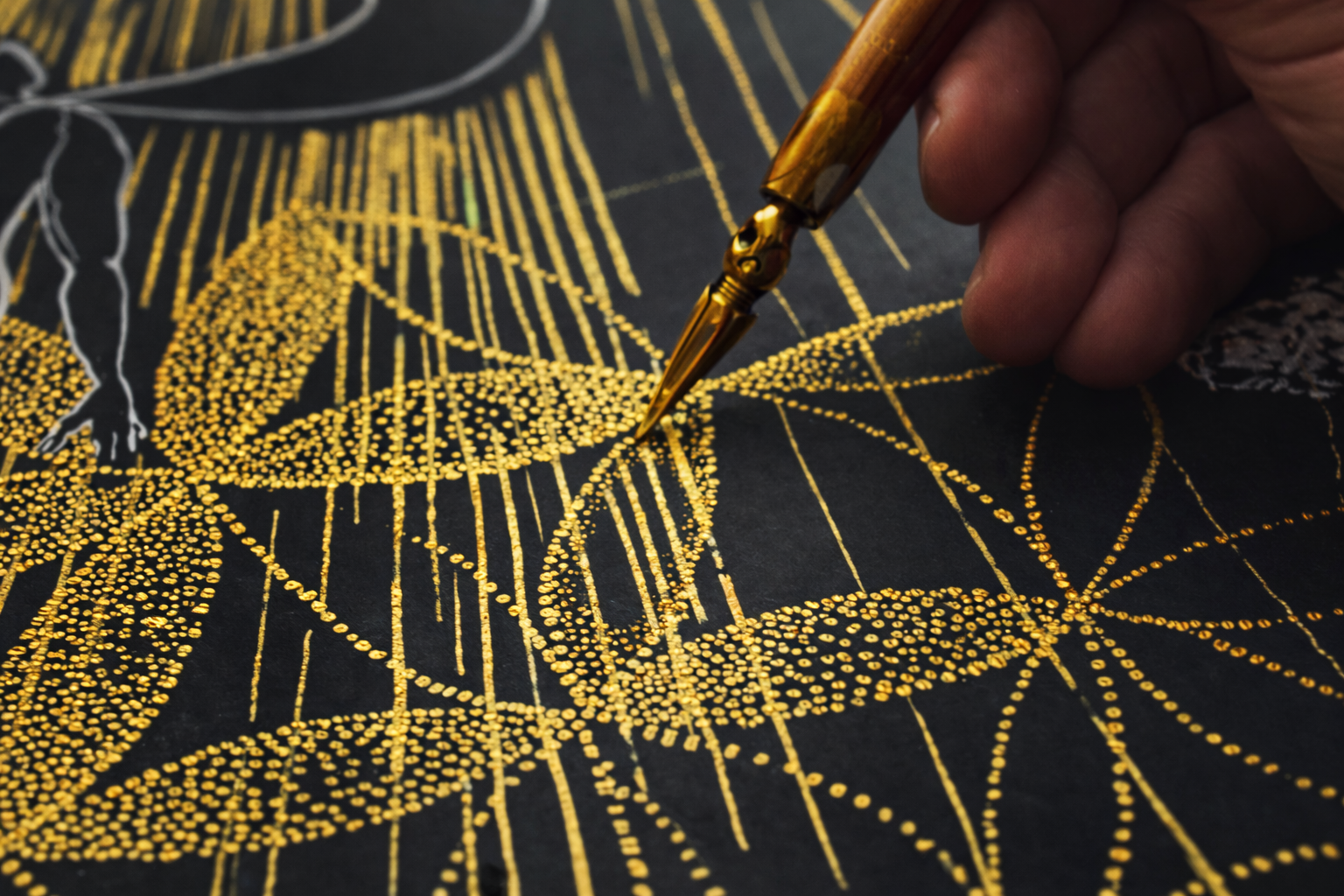 Close-up of a hand using a gold pen to create detailed gold dot art on black paper, forming a geometric flower of life pattern.